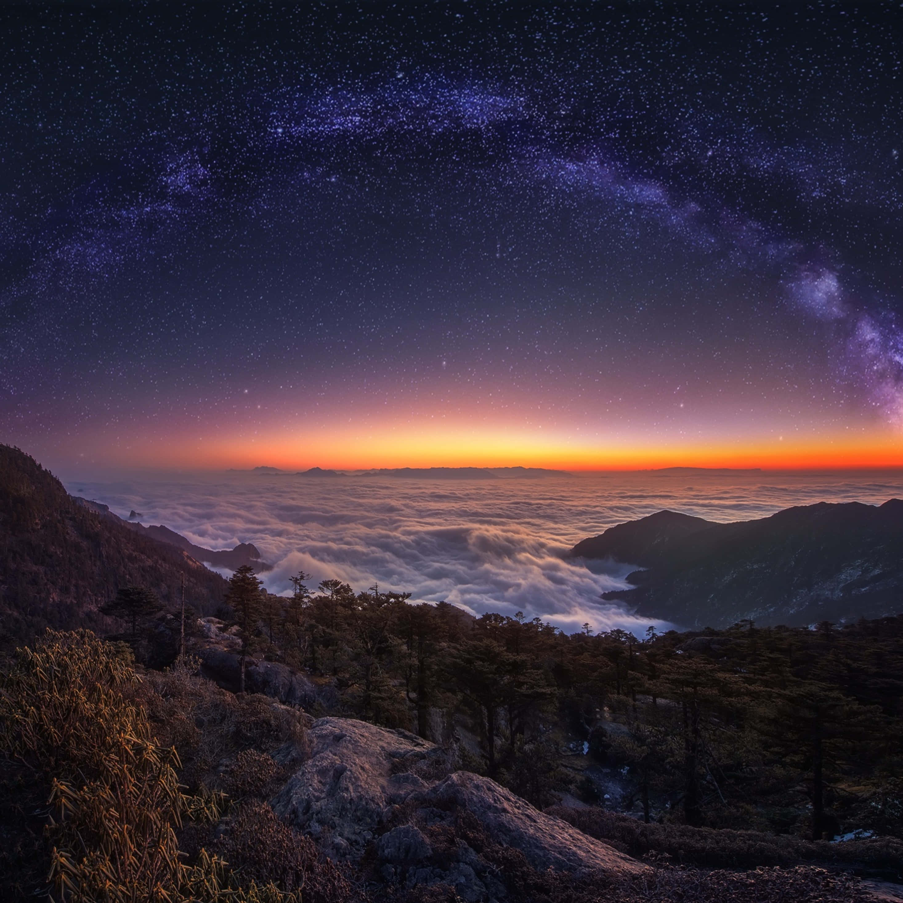 Star Sky 桌布 壁紙 — 從山脊俯瞰雲海的壯麗夜景，銀河在充滿活力的紫色和橙色天空中拱起。