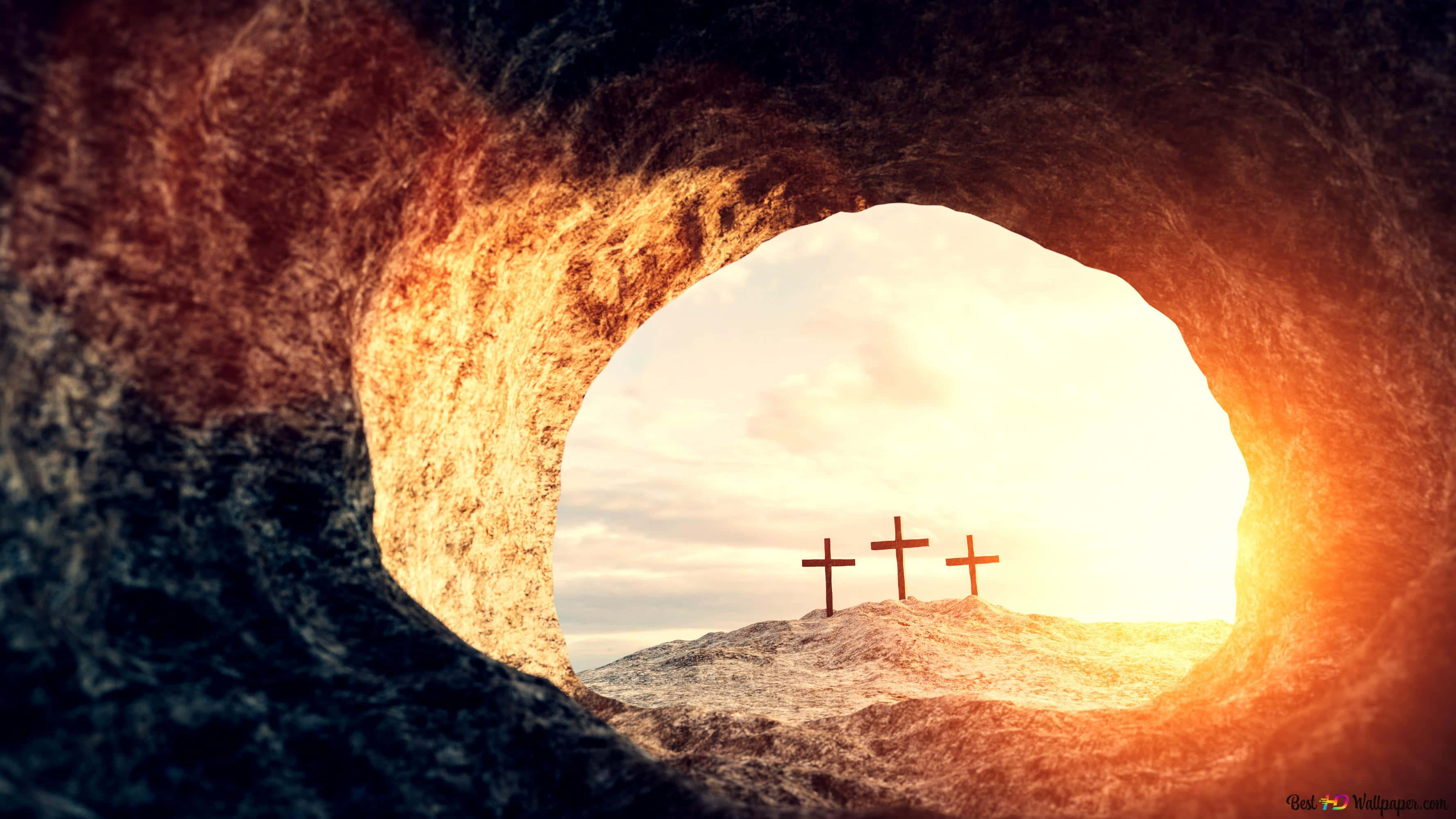 Empty Tomb 桌布 壁紙 — 從岩石墓穴開口內望向沐浴在金色日出光線中的山丘上的三個十字架的景色。
