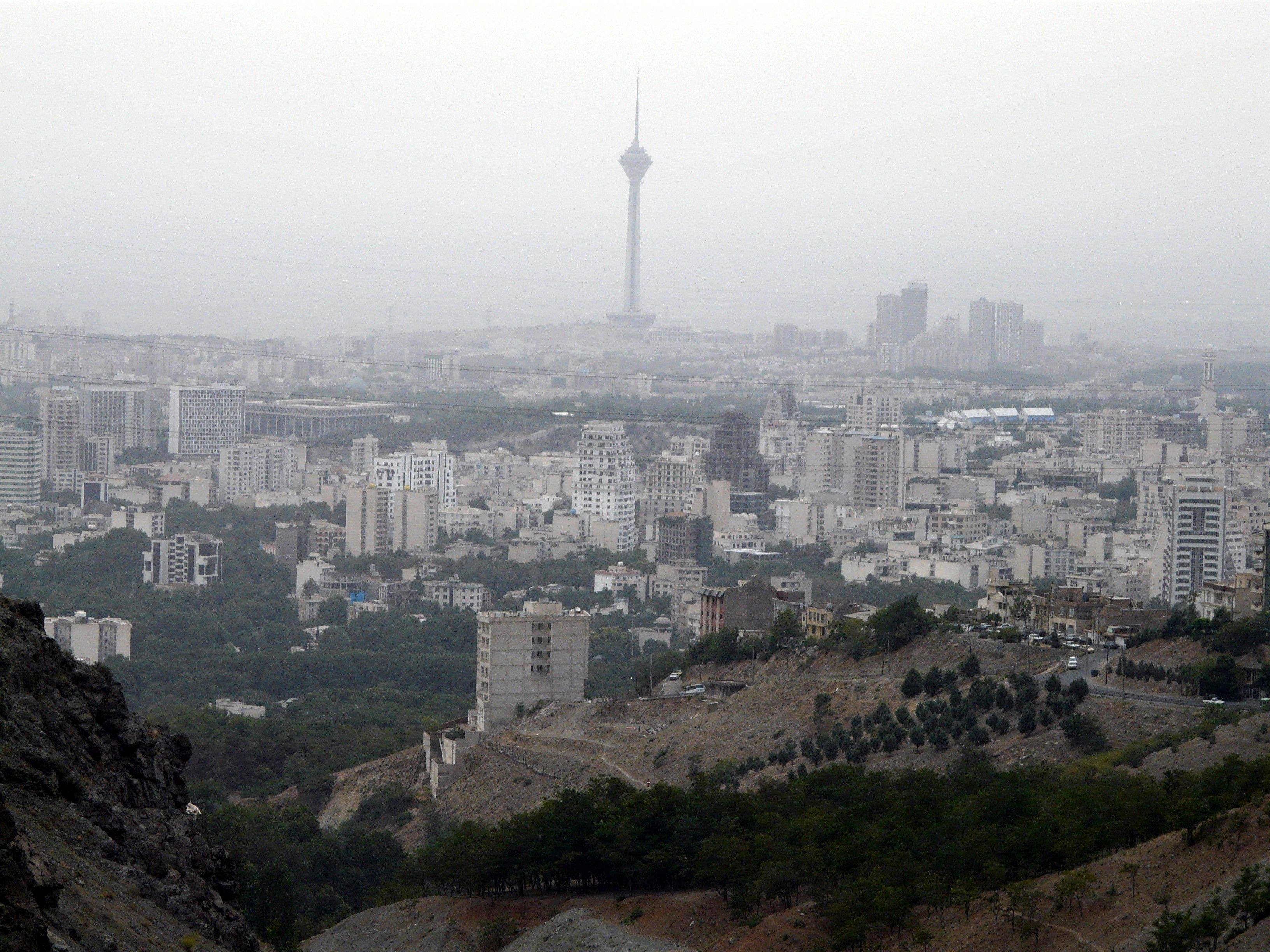 Tehran 桌布 壁紙 — 從岩石山坡上看到的朦朧城市天際線，由一座高塔主導，聳立在密集的城市景觀之上。