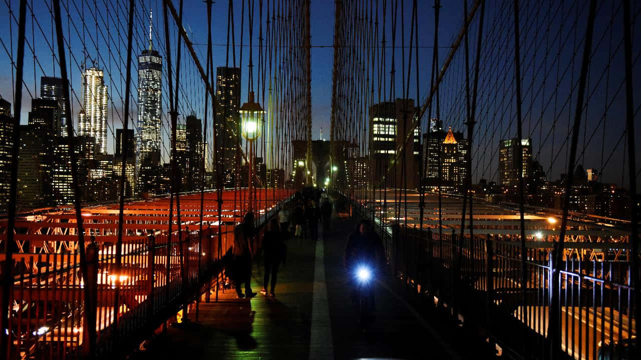 720p Ny City 桌布 壁紙 — 從布魯克林大橋欣賞夜景，城市天際線閃爍，行人走在照明懸索下。