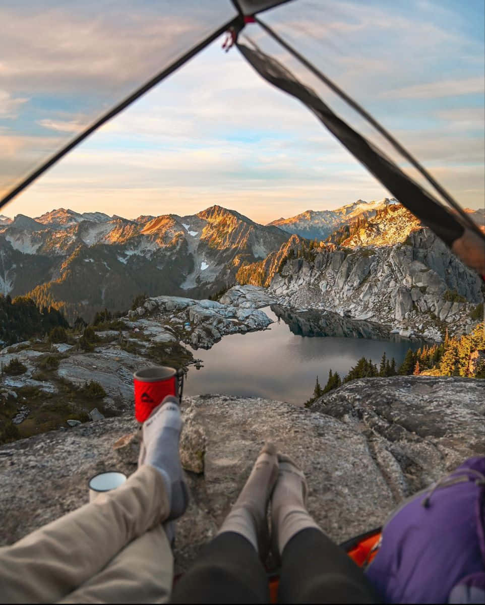 Minimalist Camping 桌布 壁紙 — 從帳篷內，雙腿伸展，俯瞰金色日落時寧靜的山間湖泊。
