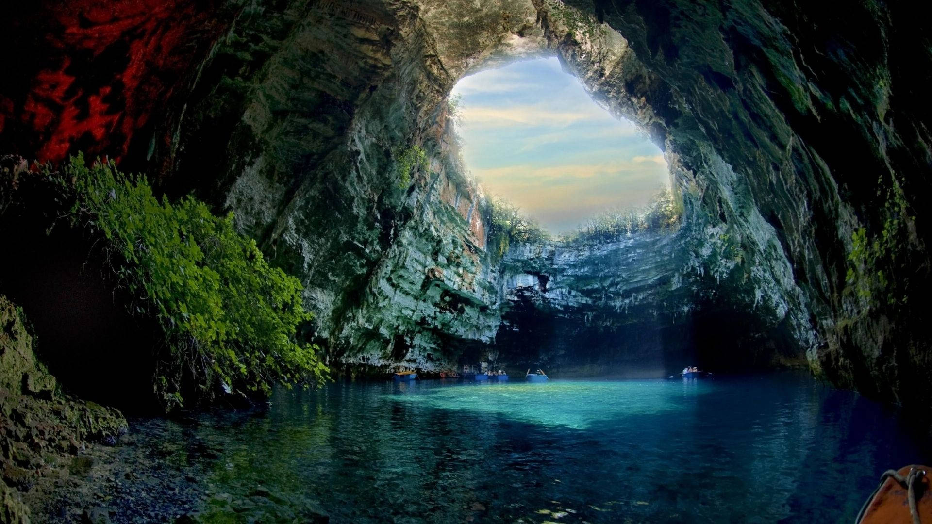 Cave 桌布 壁紙 — 從廣闊天然洞穴內部欣賞的壯麗景色，碧綠色的海水和船隻漂浮在圓形天窗下，露出柔和的藍天。