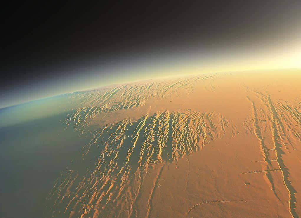 Mars Landscape 桌布 壁紙 — 從彎曲的地平線上方，火星崎嶇的赭色表面沐浴在金色陽光下的壯麗景色。
