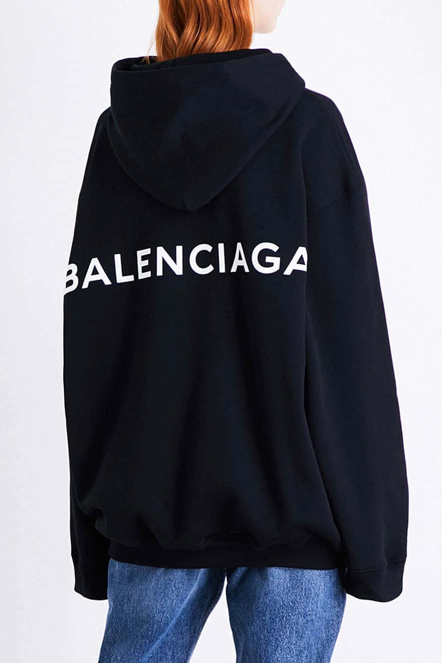 Balenciaga 桌布 壁紙 — 從後方看到一個人穿著 oversized 黑色連帽上衣，上面有粗體白色 Balenciaga 標誌，搭配藍色牛仔褲，背景為純白色。