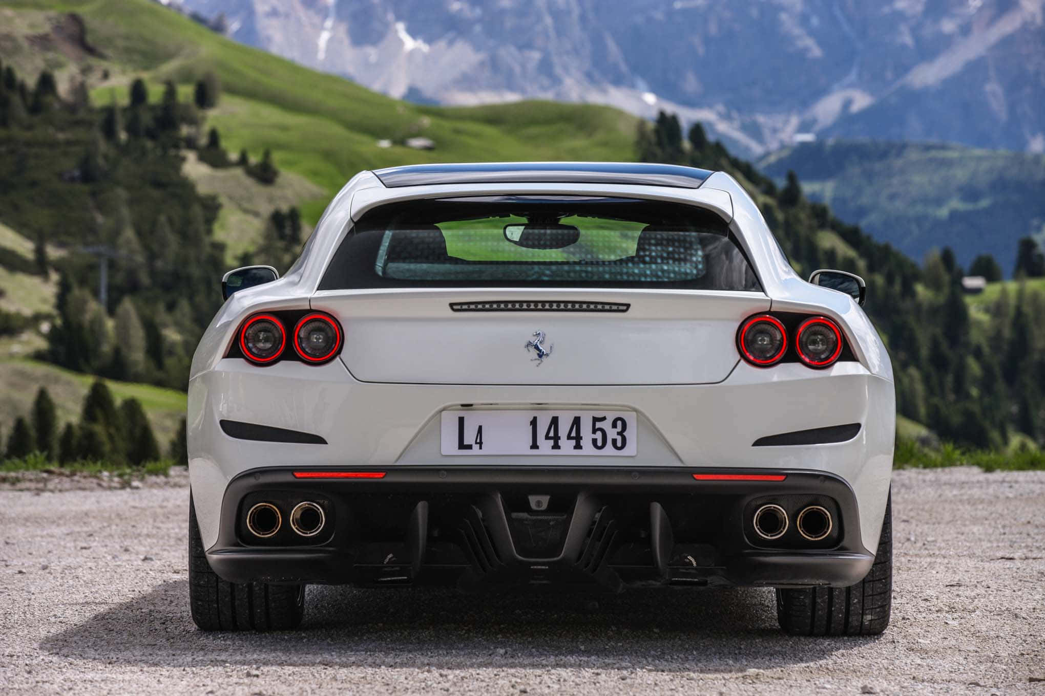 Ferrari Gtc4lusso 桌布 壁紙 — 從後方看到的白色法拉利跑車停在碎石路上，背景是白雪覆蓋的山脈和綠色山丘。