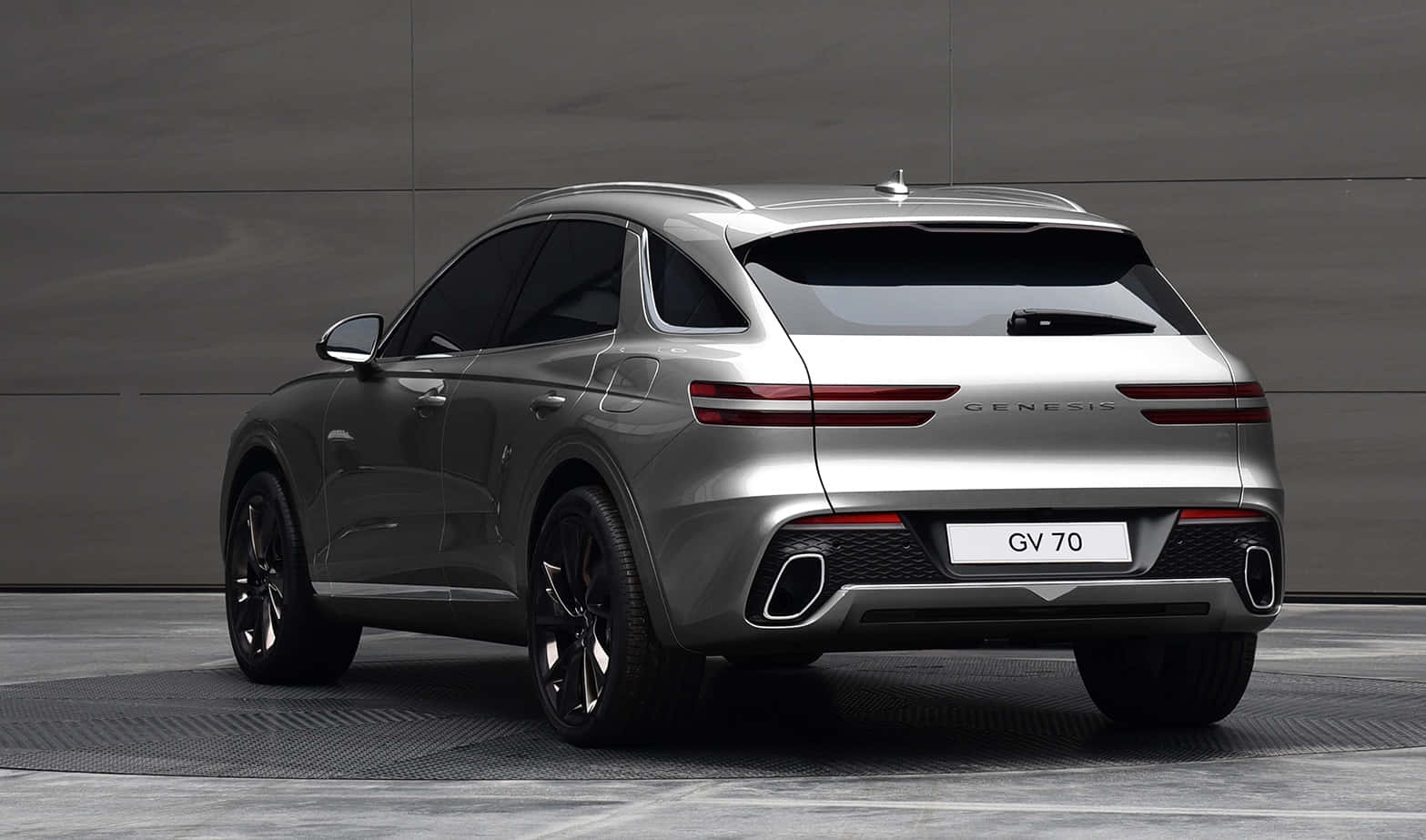 Genesis Gv70 桌布 壁紙 — 從後方觀看，一輛時尚的銀色 Genesis GV70 SUV 停在簡約灰色混凝土牆前。