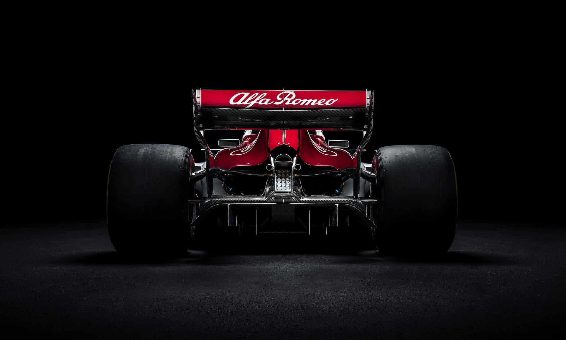 Racing 桌布 壁紙 — 從後方觀看，一輛流線型紅色愛快羅密歐一級方程式賽車，背景為黑色，燈光效果戲劇化。