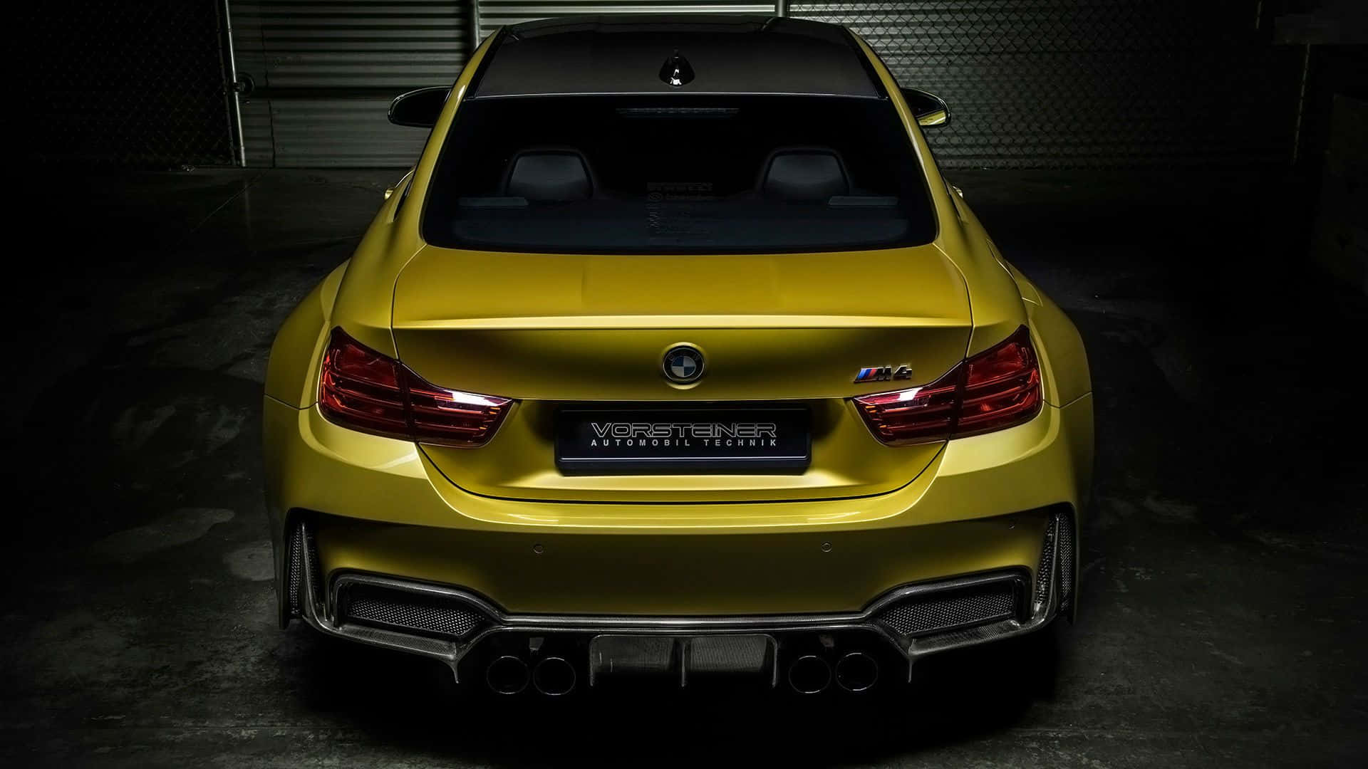 BMW 動圖 桌布 壁紙 — 從後方觀看一輛光澤黃色、經Vorsteiner改裝的BMW M4雙門轎跑車，位於光線昏暗的車庫中，帶有戲劇性照明。