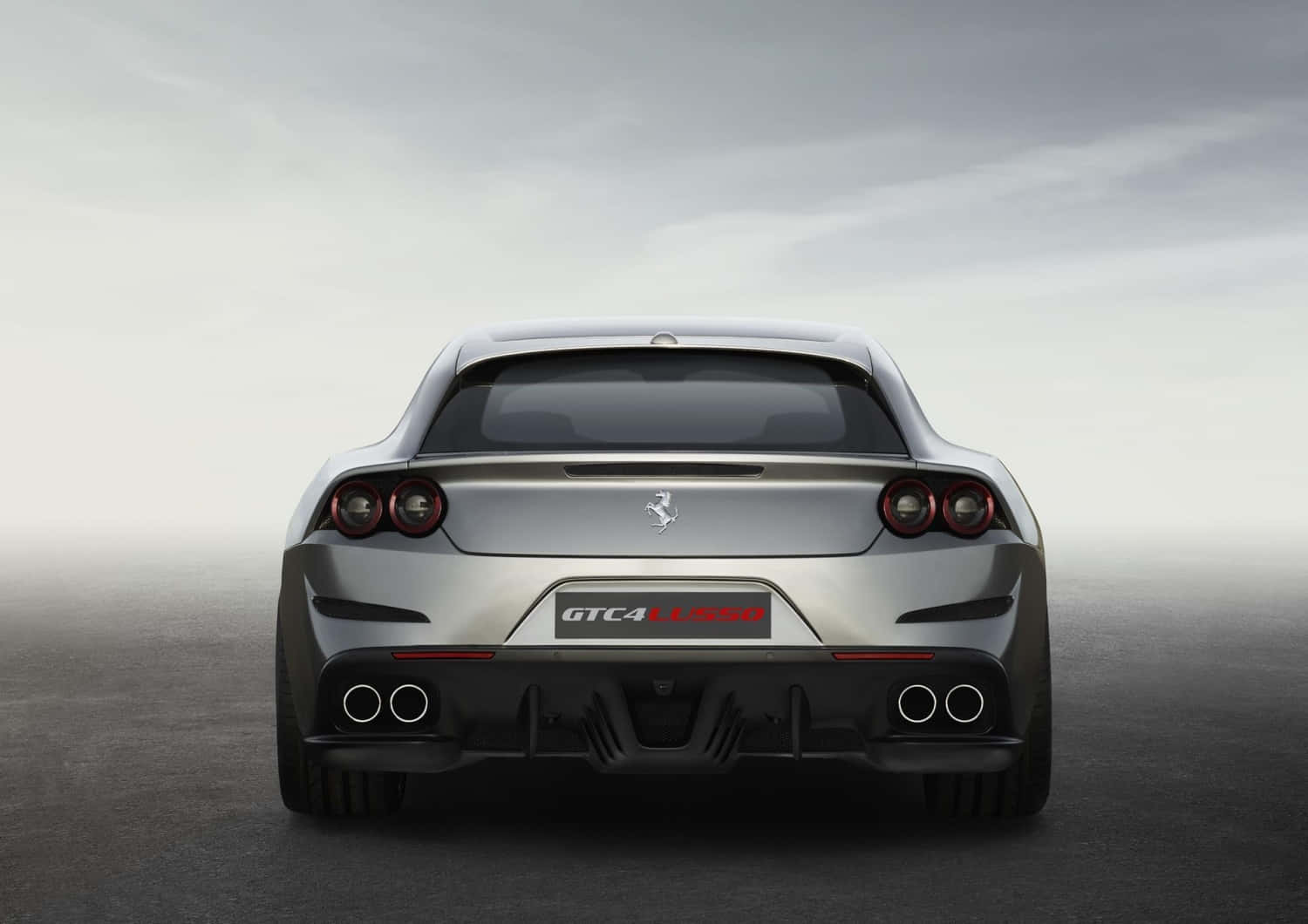 Ferrari Gtc4lusso 桌布 壁紙 — 從後方觀看一輛流線型銀色法拉利 GTC4Lusso，背景是朦朧的灰色天空和霧氣瀰漫的地面。