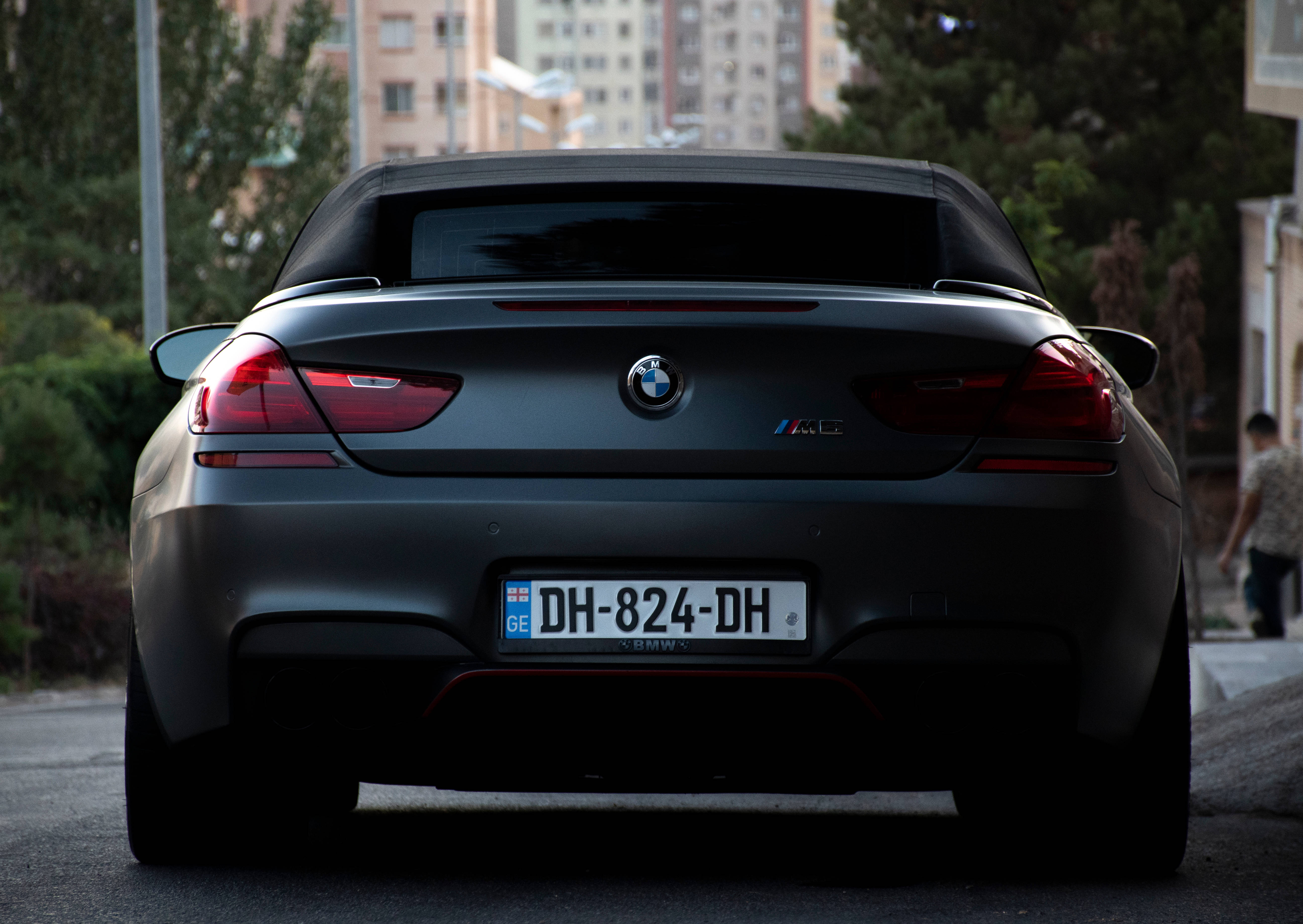 m 桌布 壁紙 — 從後方觀看一輛消光黑色BMW M6敞篷車停放在城市的街道上，背景有樹木和建築物。