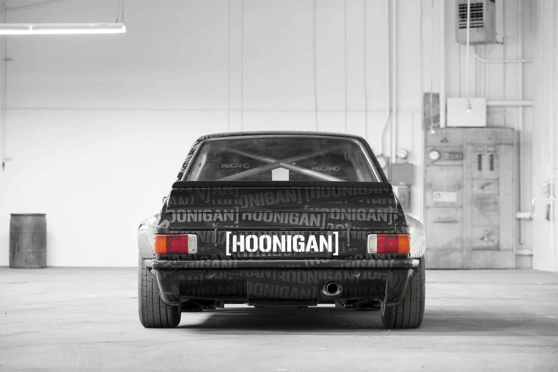 Ken Block 桌布 壁紙 — 從後方觀看一輛黑色Hoonigan改裝車停放在單色調的簡陋工業車庫中。
