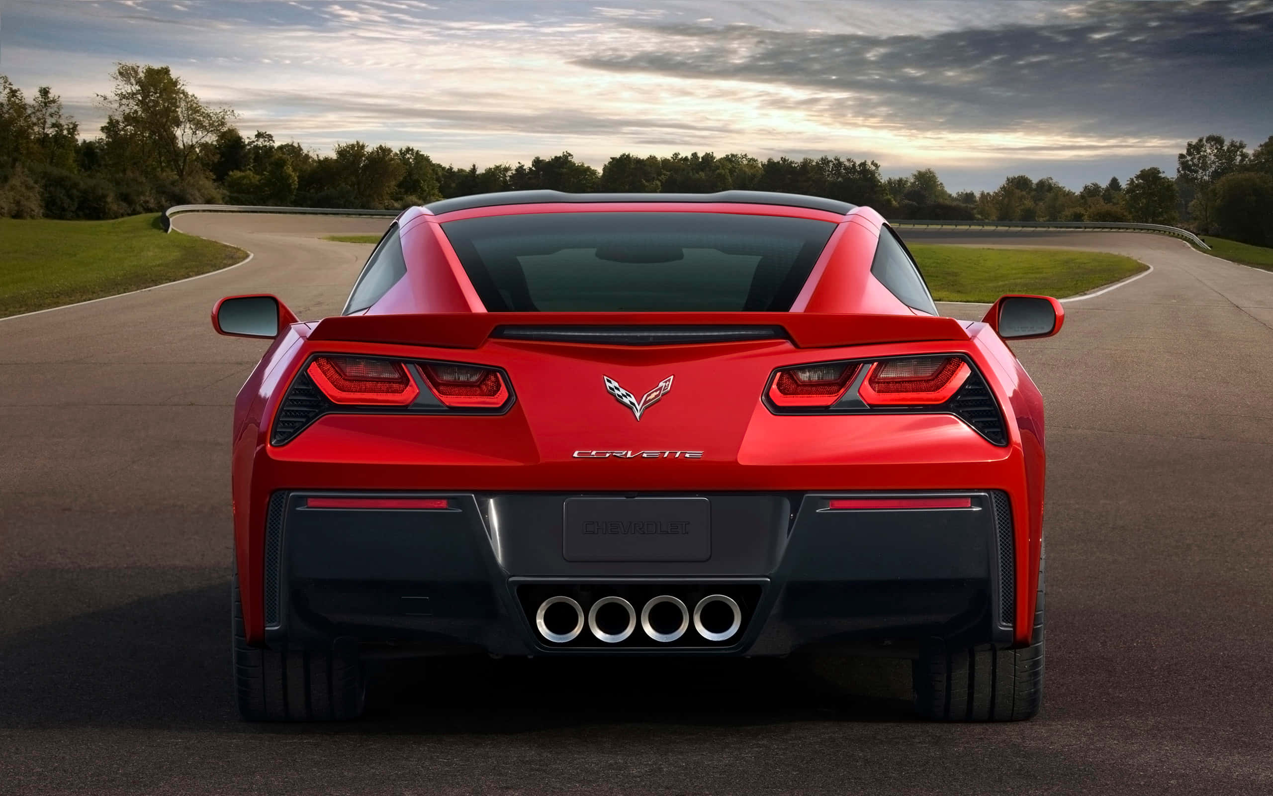 Chevrolet Corvette Stingray 桌布 壁紙 — 從後面看，一輛鮮紅色的雪佛蘭克爾維特跑車在日落時分行駛在蜿蜒的道路上。
