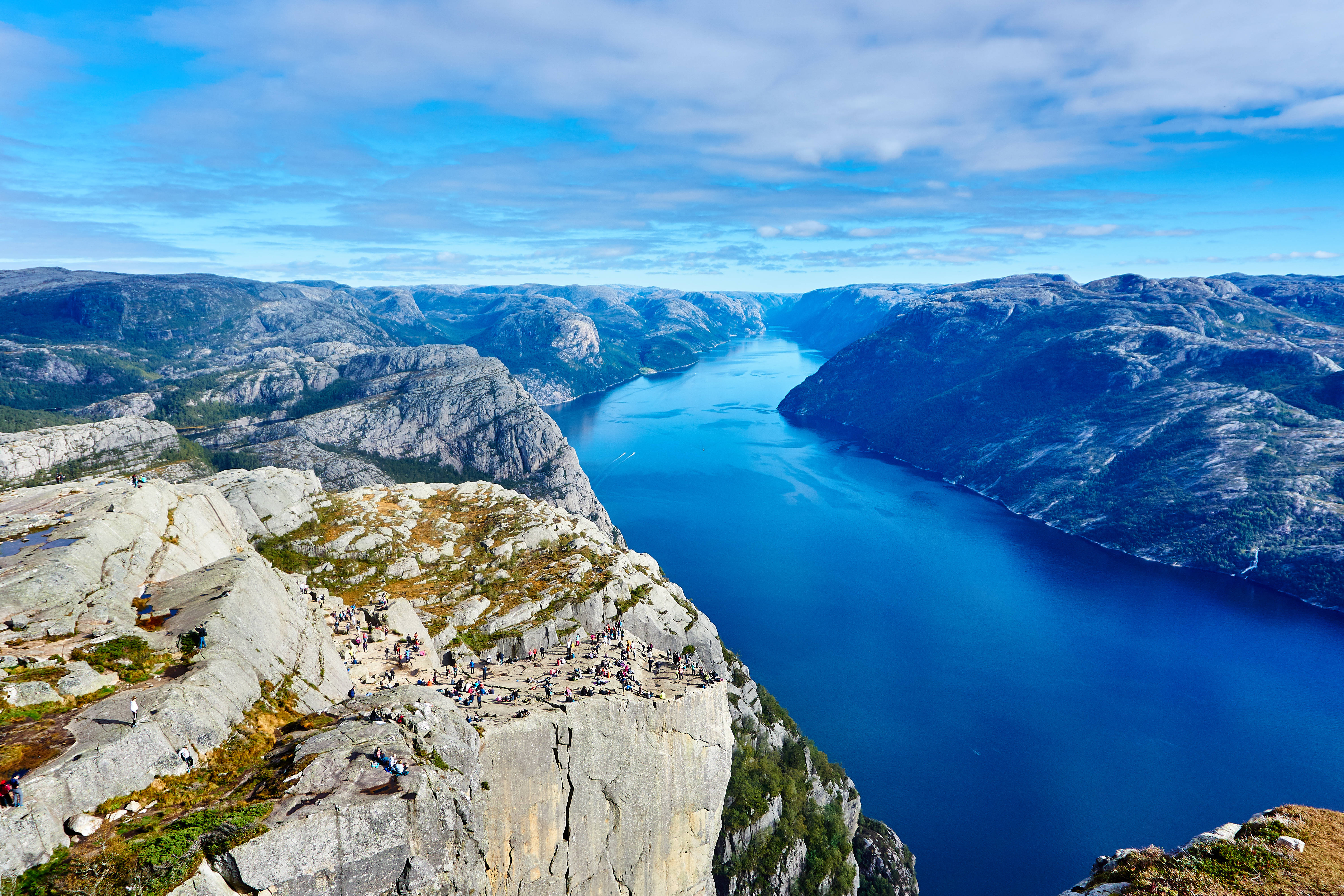 Norway 桌布 壁紙 — 從懸崖邊緣俯瞰深藍色峽灣的壯麗全景，峽灣兩側是崎嶇的山脈，天空部分多雲。