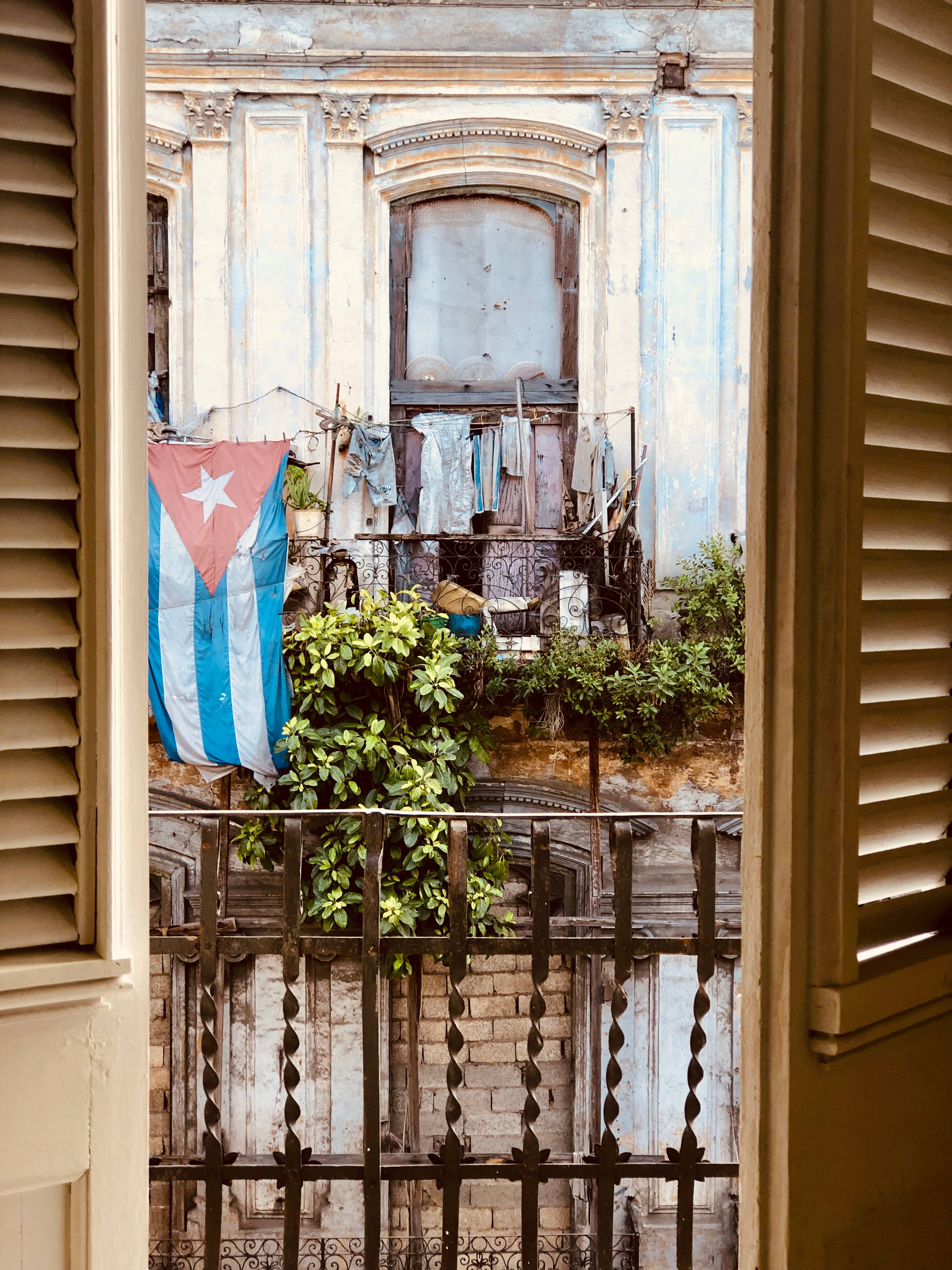 Cuba 桌布 壁紙 — 從打開的木百葉窗望去，一面飽經風霜的古巴國旗懸掛在破舊殖民建築的陽台上。