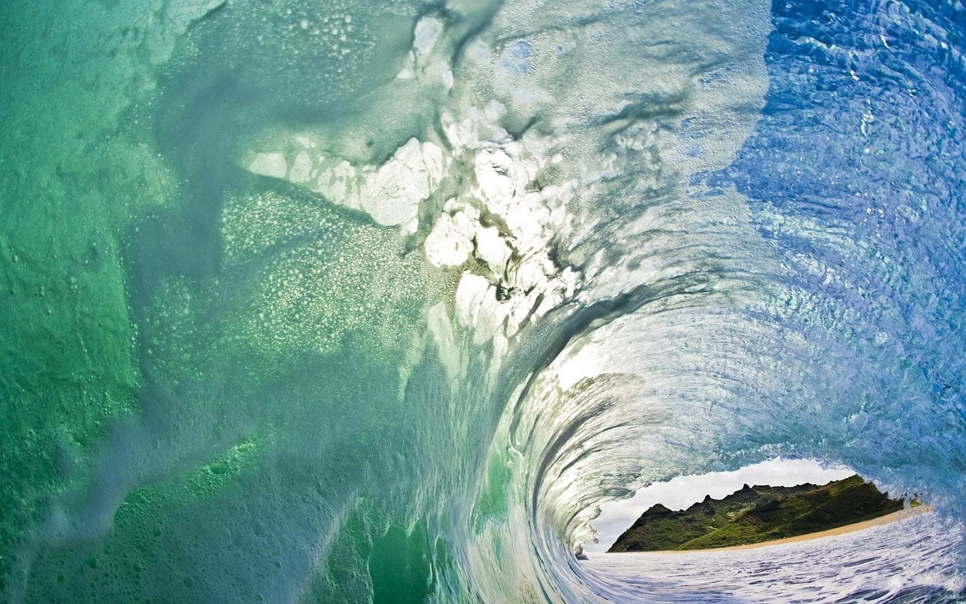 Ocean Waves 桌布 壁紙 — 從捲曲海浪內部看到的驚人水下景觀，顯露出遠方一個綠色島嶼海灘。