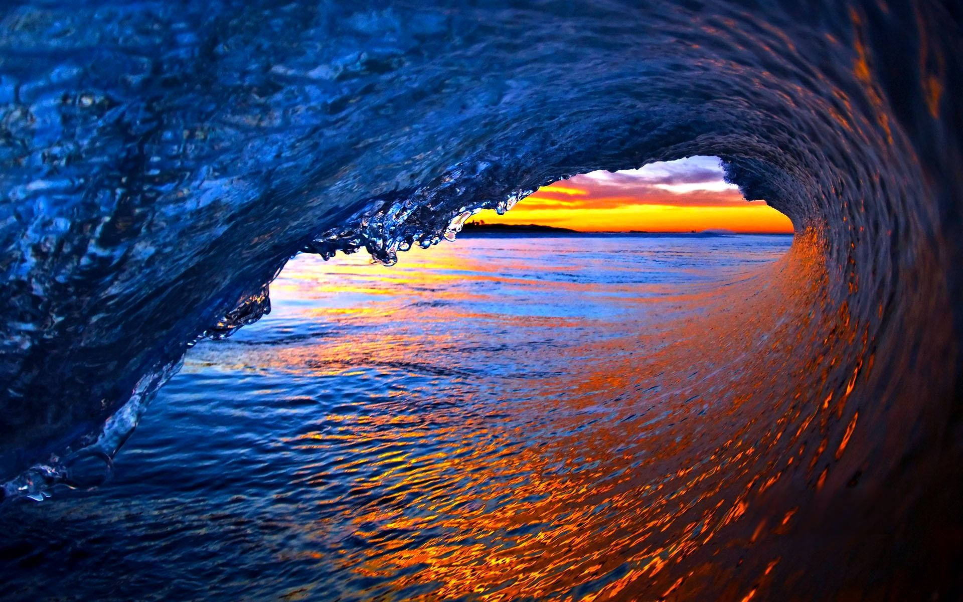 Wave 桌布 壁紙 — 從捲曲的海浪內部欣賞日落時分的壯麗景色，帶有鮮豔的藍色和橙色反射。