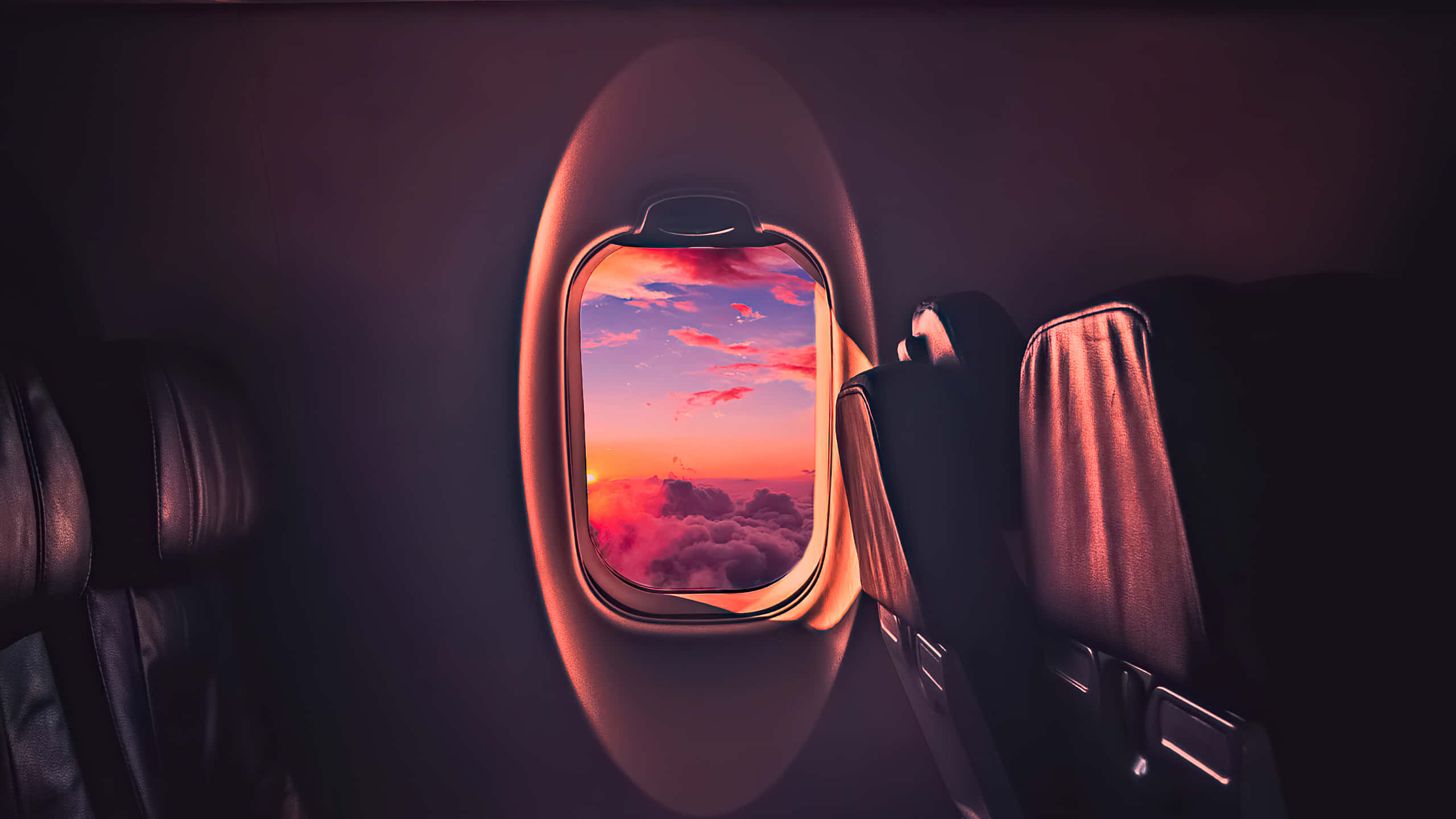 1440p Amoled 桌布 壁紙 — 從昏暗機艙內看到的飛機窗外景觀，蓬鬆雲朵上 vibrant 粉紅與橙色日落。