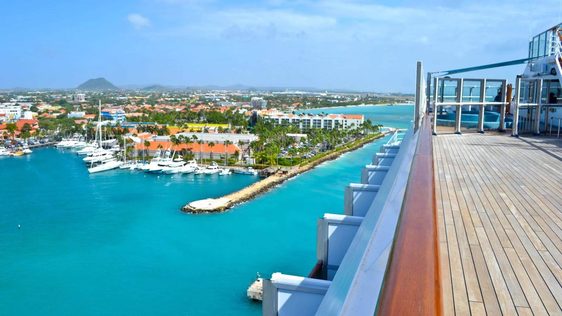 Aruba 桌布 壁紙 — 從木製郵輪甲板上看到的充滿遊艇和棕櫚樹的充滿活力的藍綠色港口，天空清澈湛藍。