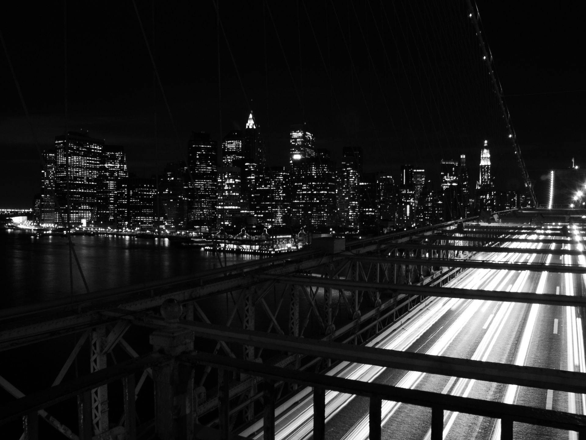 New York 桌布 壁紙 — 從橋上拍攝的黑白夜景，顯示交通的光軌和水面上發光的城市天際線。