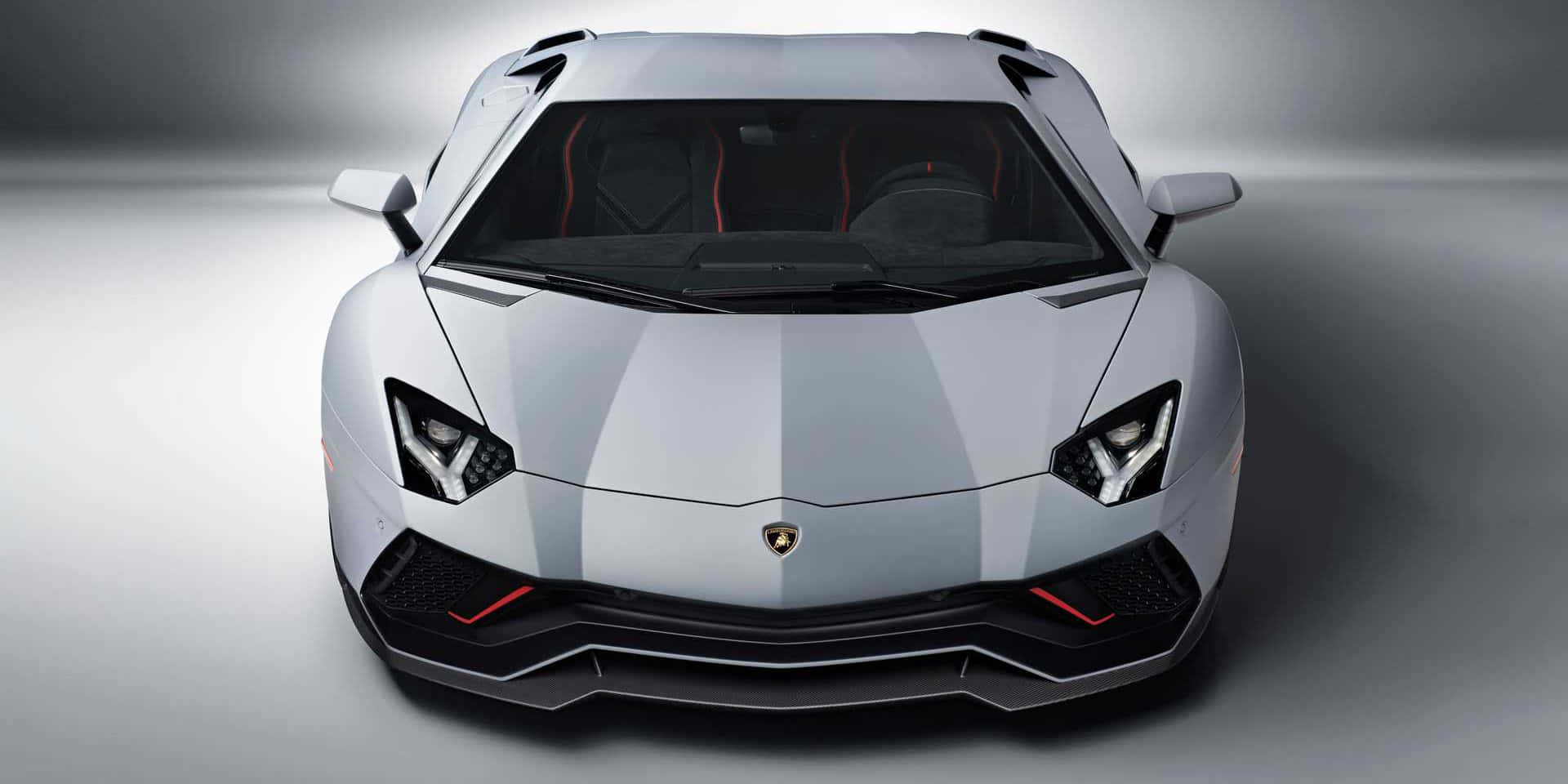跑車 桌布 壁紙 — 從正面觀看一輛時尚的銀色藍寶堅尼Aventador超級跑車，具有銳利的棱角線條和發光的紅色點綴，背景為簡約的工作室。