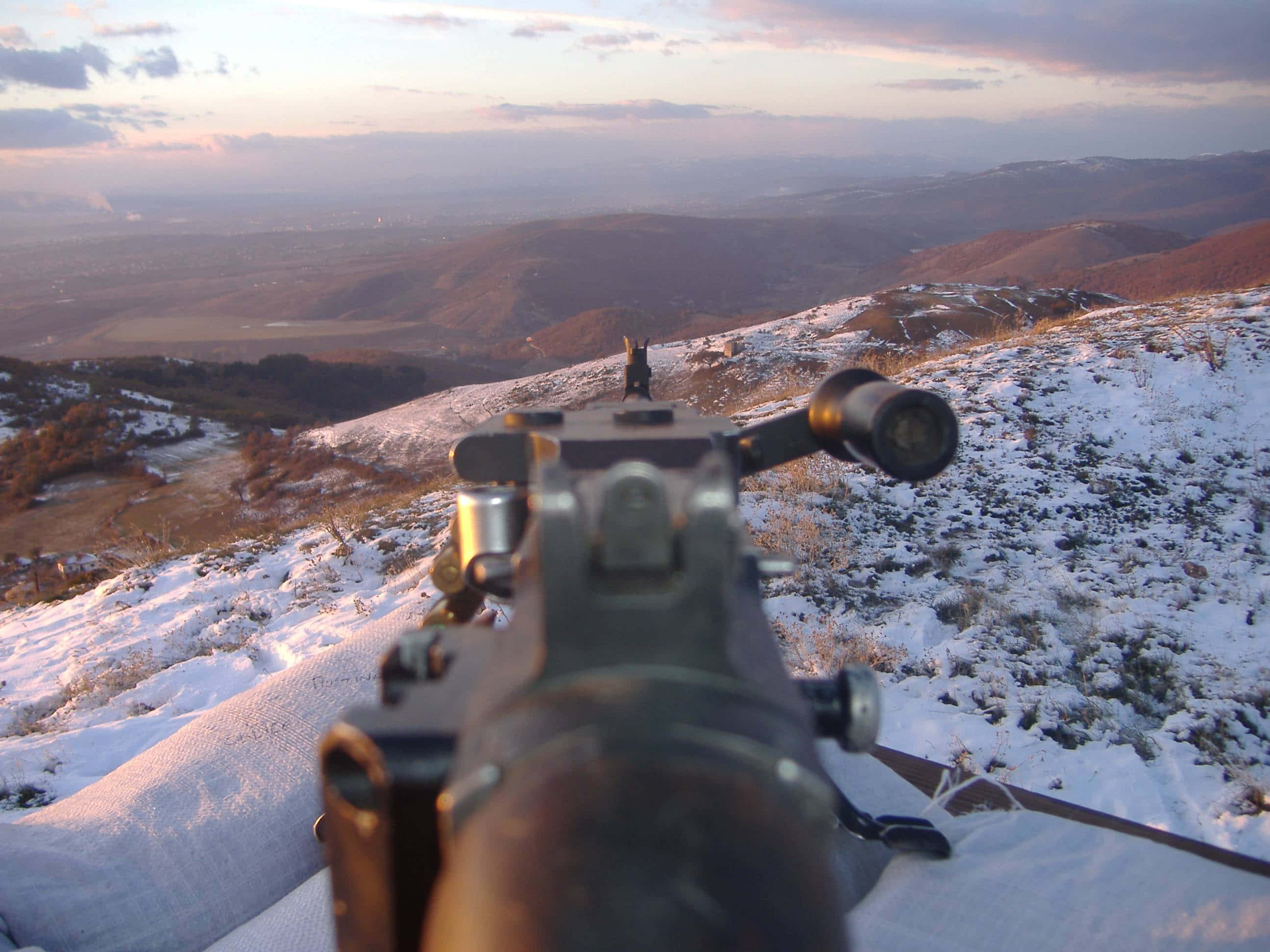 Rifle 桌布 壁紙 — 從步槍的第一人稱視角，位於白雪覆蓋的山丘頂部，俯瞰廣闊的山谷，夕陽西下。