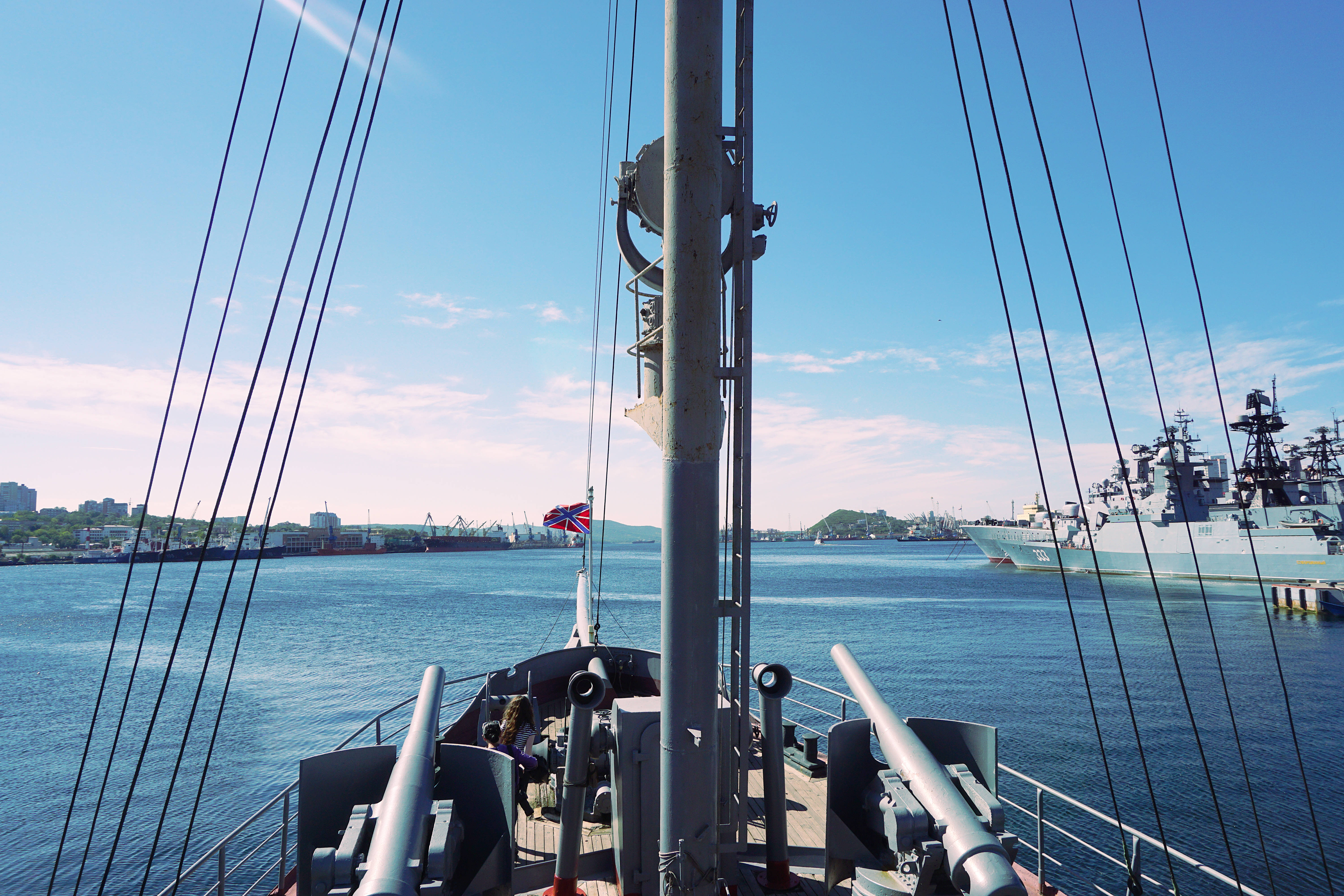 Warship 桌布 壁紙 — 從歷史戰艦甲板上的景色，展示大砲、索具和英國國旗，以明亮的藍天為背景，港口內有其他海軍艦艇。