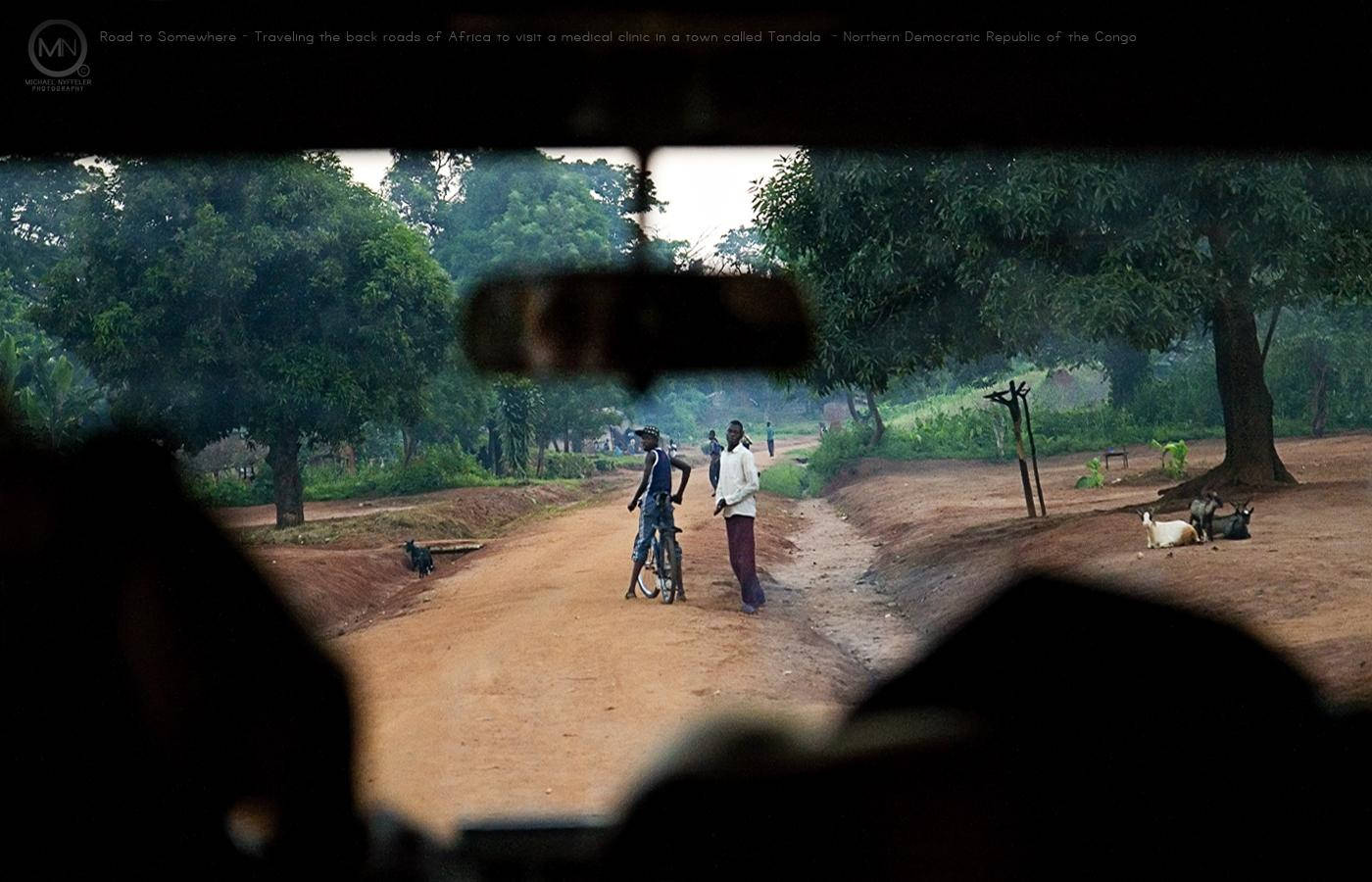 Congo 桌布 壁紙 — 從汽車擋風玻璃望出去，顯示在非洲鄉村一條穿過茂密綠樹的泥路上有兩個人和山羊。