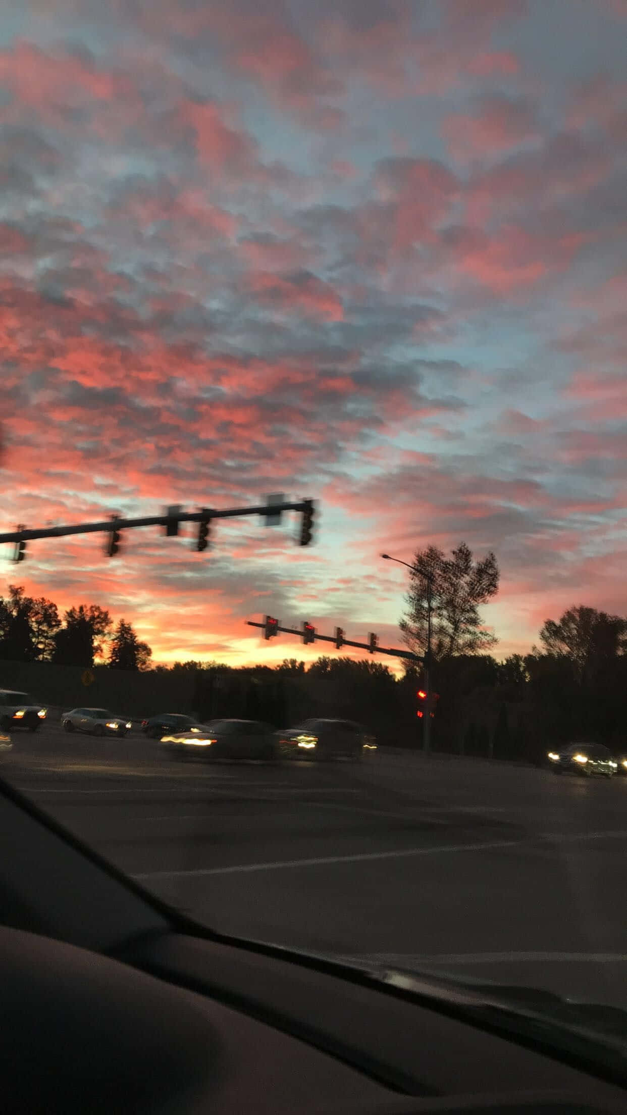 桌布 壁紙 — 從汽車擋風玻璃觀看繁忙十字路口上充滿活力的粉紅色和橙色日落，有交通燈和行駛中的汽車。