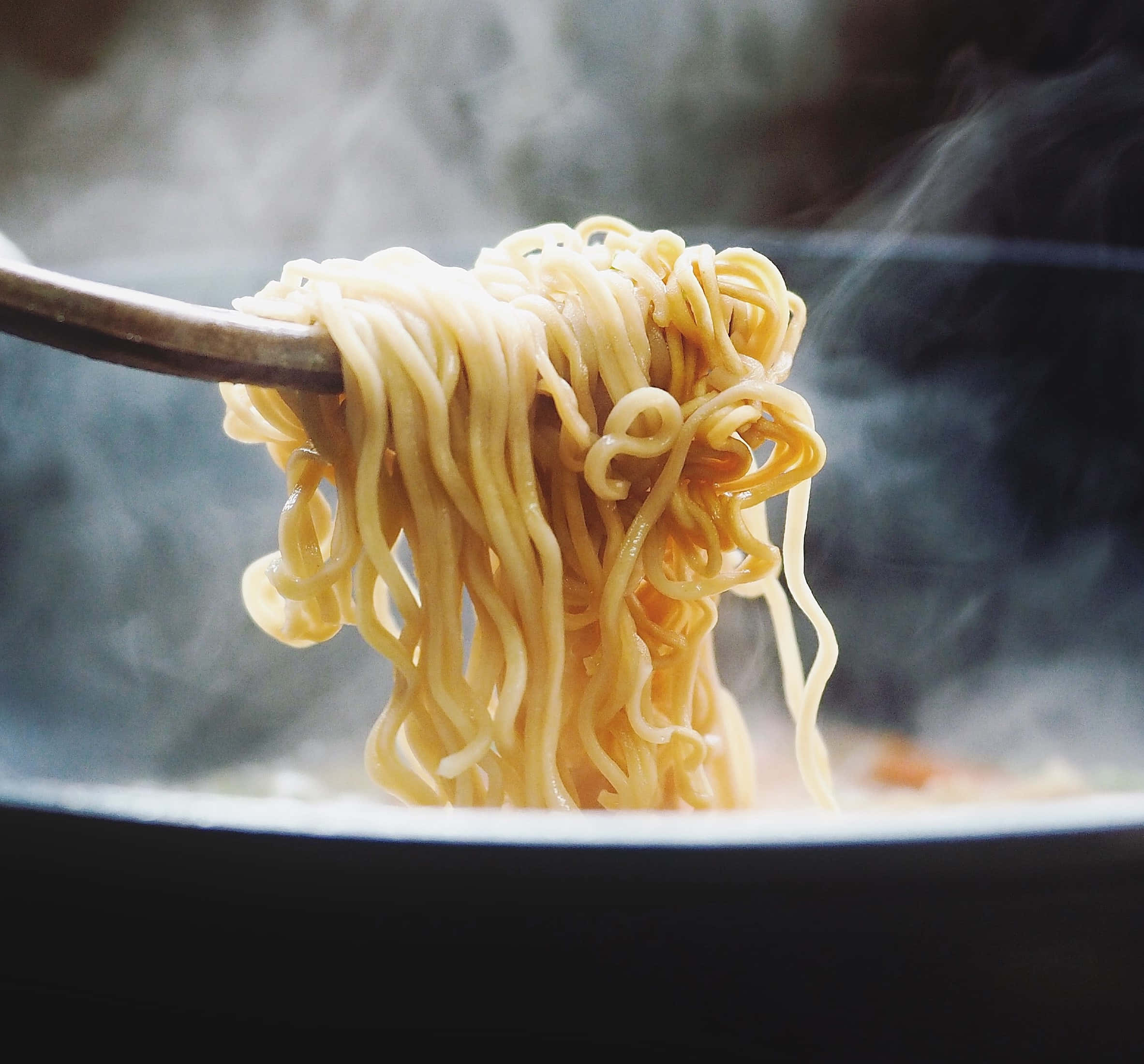 Food Photography 桌布 壁紙 — 從熱碗中用筷子夾起冒煙的麵條，蒸氣在模糊的背景中升起。