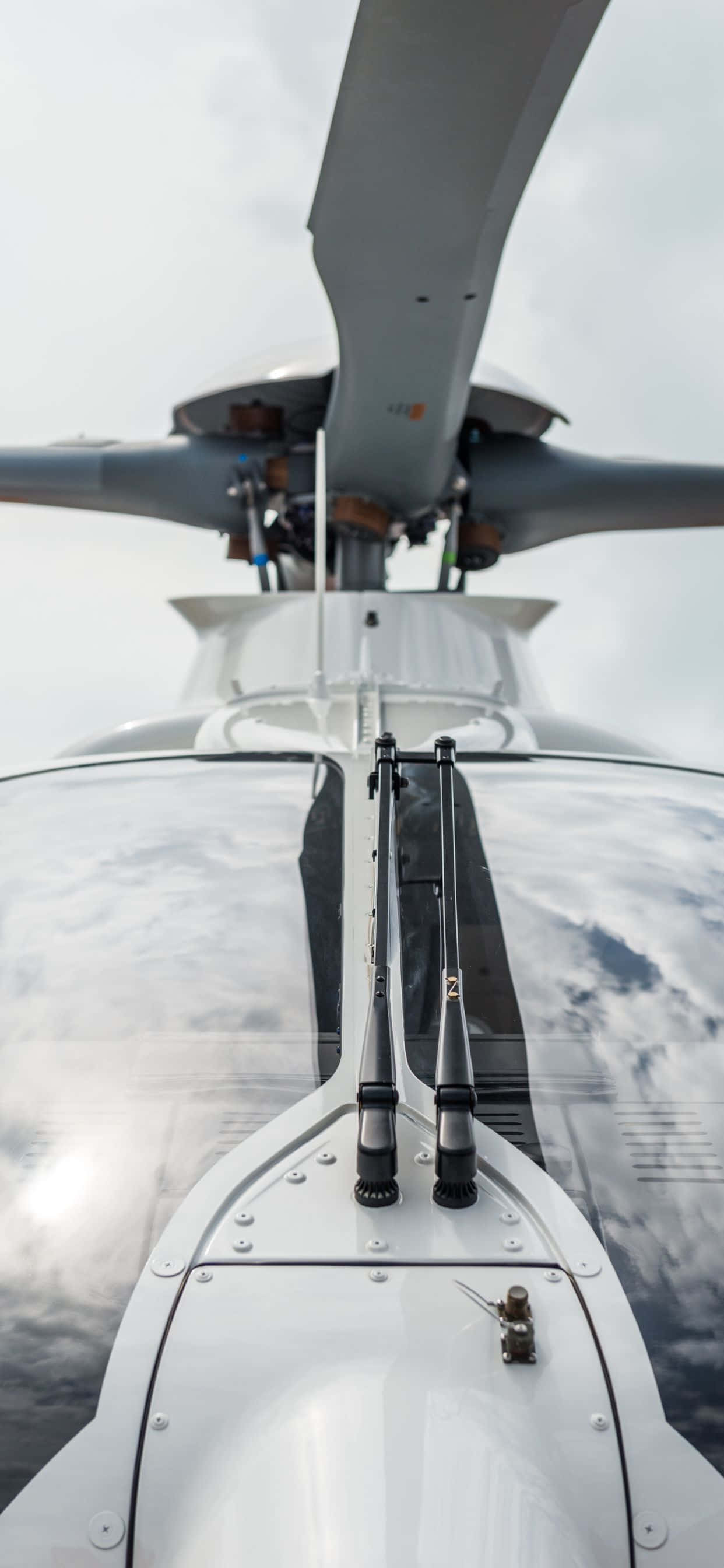 iPhone Xs Max Helicopters 桌布 壁紙 — 從直升機駕駛艙內的低角度視角，仰望旋翼葉片，背景是陰雲密布的天空。