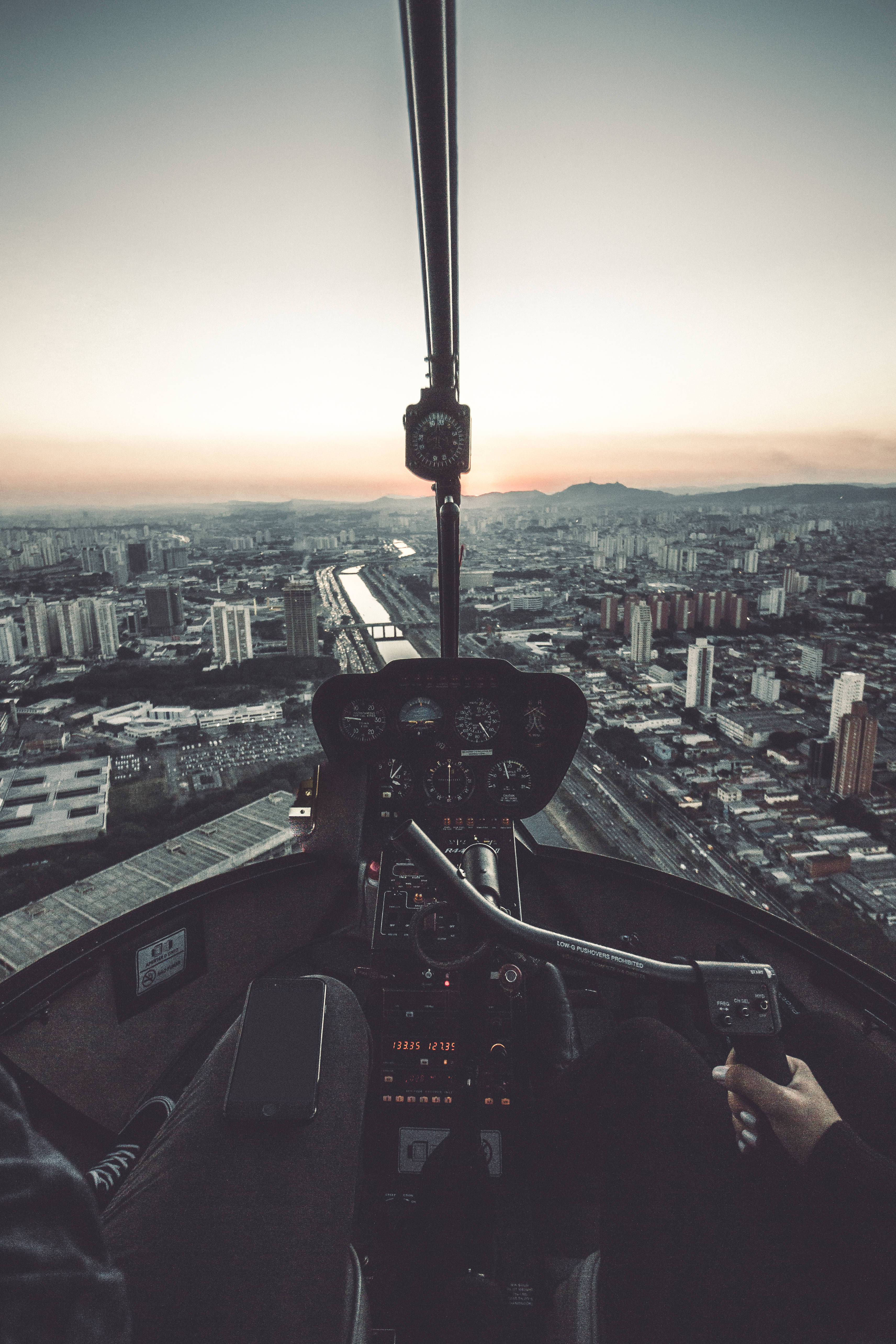 Helicopter 桌布 壁紙 — 從直升機駕駛艙在日落時分俯瞰廣闊城市和遠處山脈的飛行員視角。