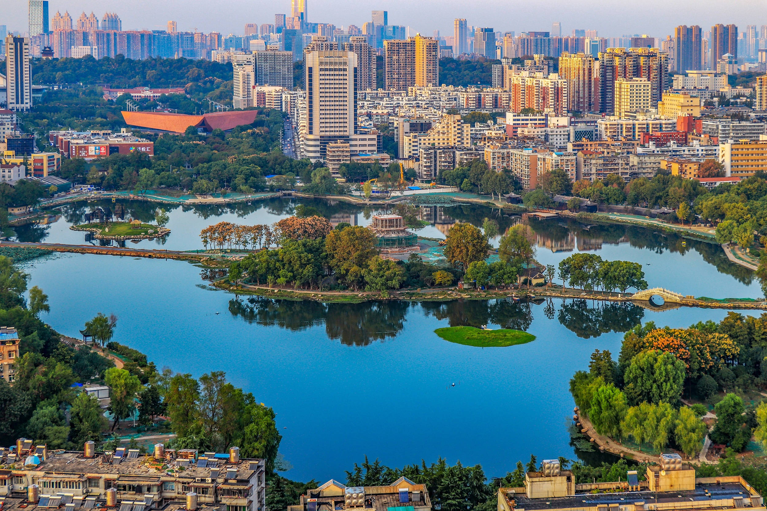 Guangzhou 桌布 壁紙 — 從空中俯瞰，一個寧靜的城市湖泊被茂密的綠化和現代高層建築環繞，沐浴在柔和的金色時光中。