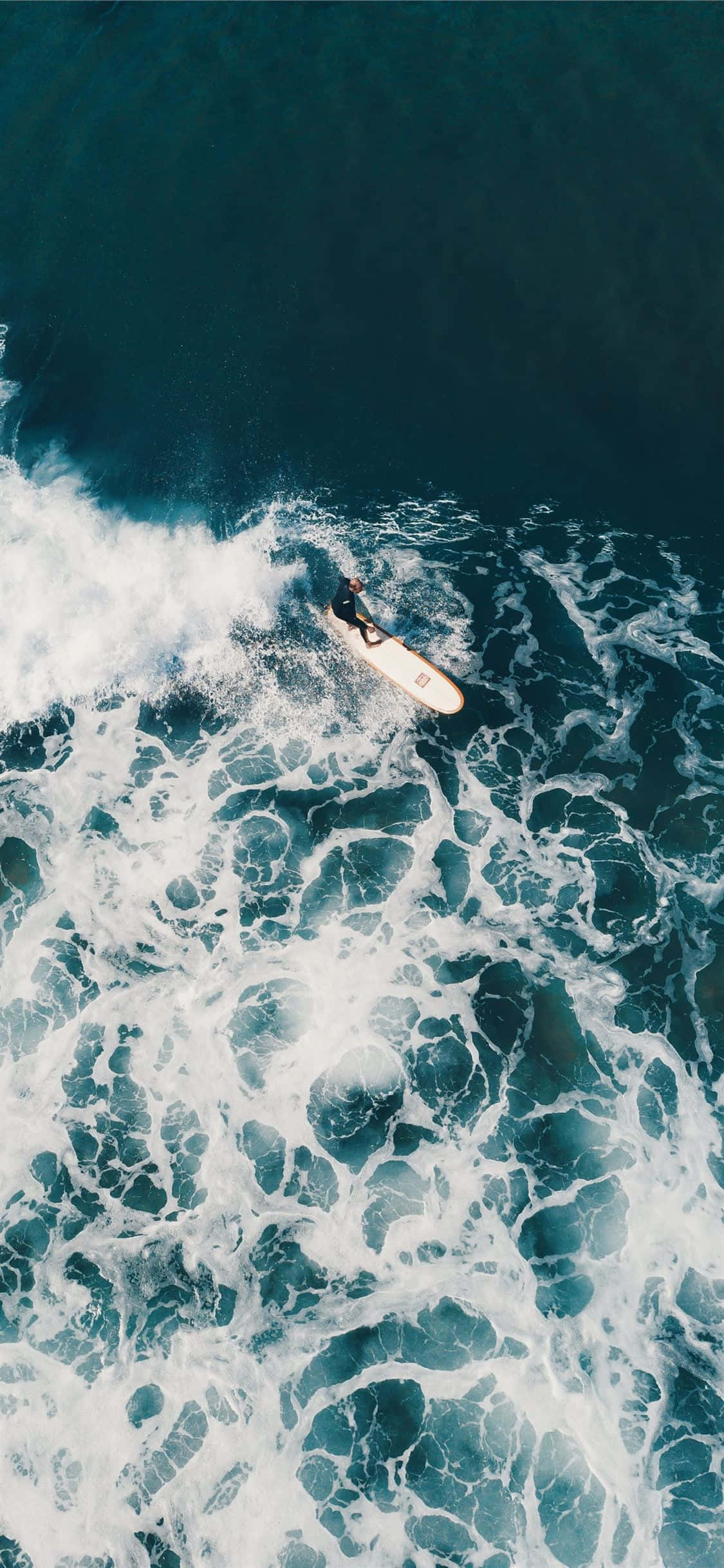 Surfing iPhone 桌布 壁紙 — 從空中俯瞰，一名衝浪者在深藍色海水上騎乘泡沫海浪。