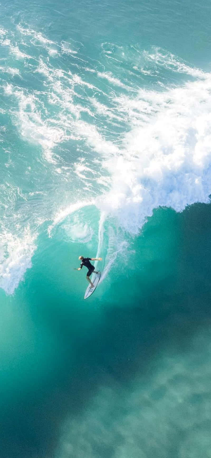 Ocean Aesthetic Phone 桌布 壁紙 — 從空中俯瞰，一名衝浪者騎乘著巨大的藍綠色海浪，周圍白色泡沫四濺。