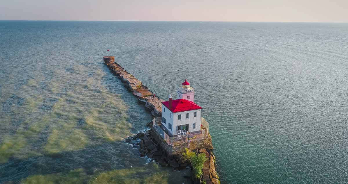 Lake Erie 桌布 壁紙 — 從空中俯瞰，一座白色燈塔帶紅色屋頂矗立在岩石海岸上，由石碼頭連接到平靜的碧綠海水，在柔和日光下。