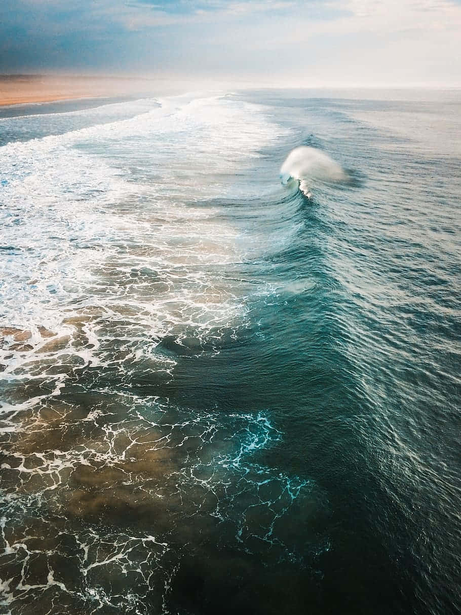 Surfing iPhone 桌布 壁紙 — 從空中俯瞰，一道強勁的海浪完美捲成筒狀，帶著泡沫般的白色海水，映襯著朦朧的地平線。