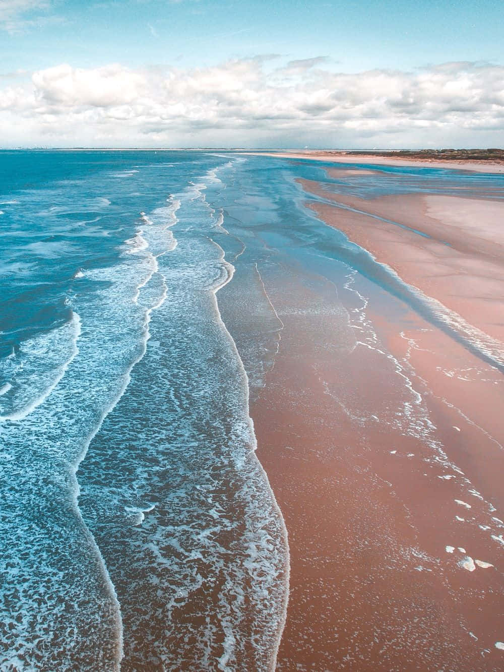 Beach Scene 桌布 壁紙 — 從空中俯瞰，在部分多雲的天空下，碧綠色的海浪輕輕拍打著充滿活力的粉紅色沙灘。