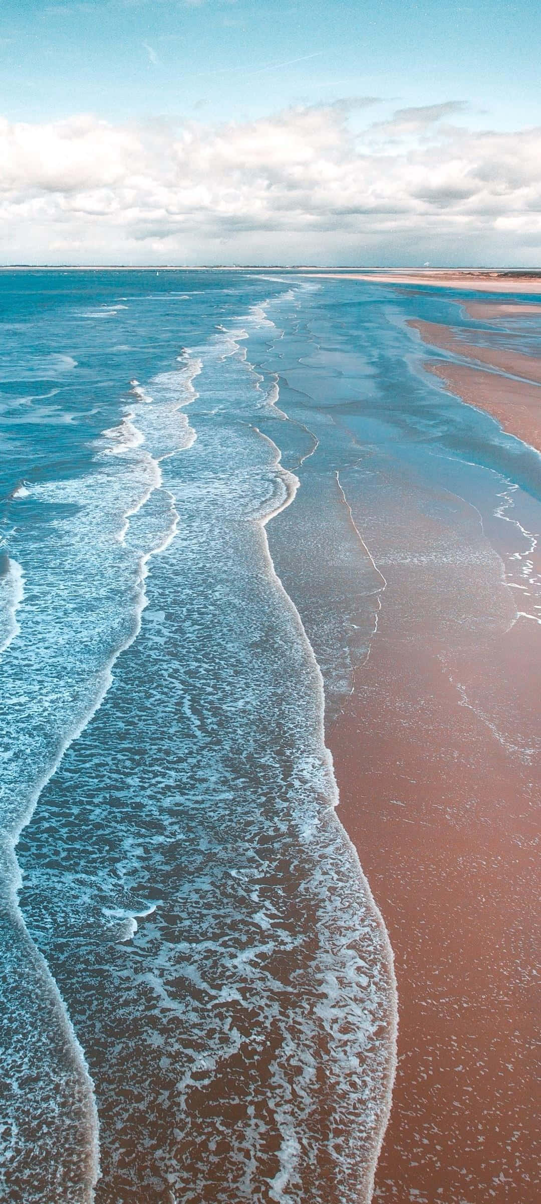 waves 桌布 壁紙 — 從空中俯瞰，在部分多雲的天空下，碧綠色的海浪拍打著紅褐色的沙灘。