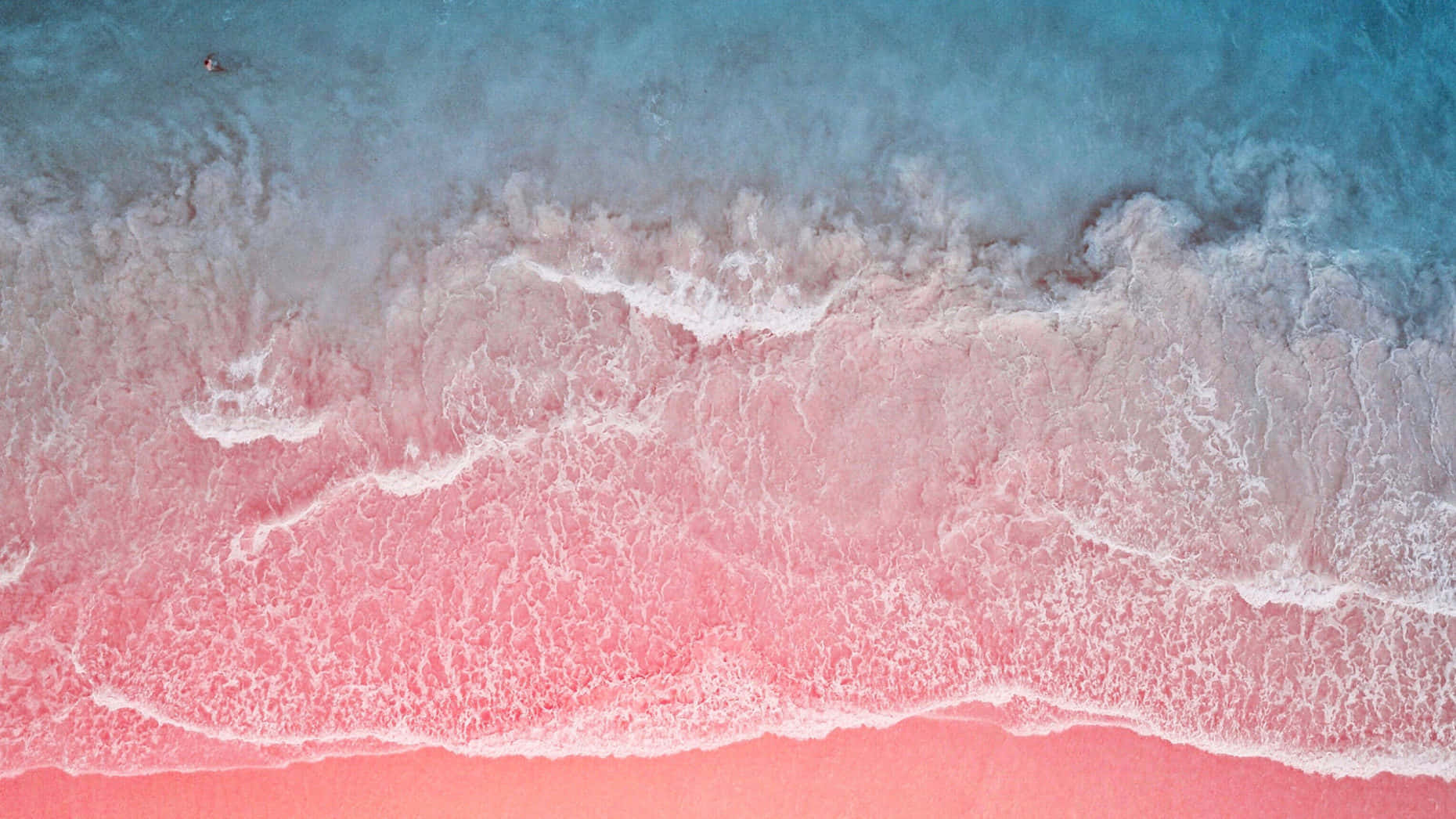 Pink Sand Beach 桌布 壁紙 — 從空中俯瞰，碧綠色的海浪拍打著充滿活力的粉紅色沙灘，激起白色泡沫般的浪花。