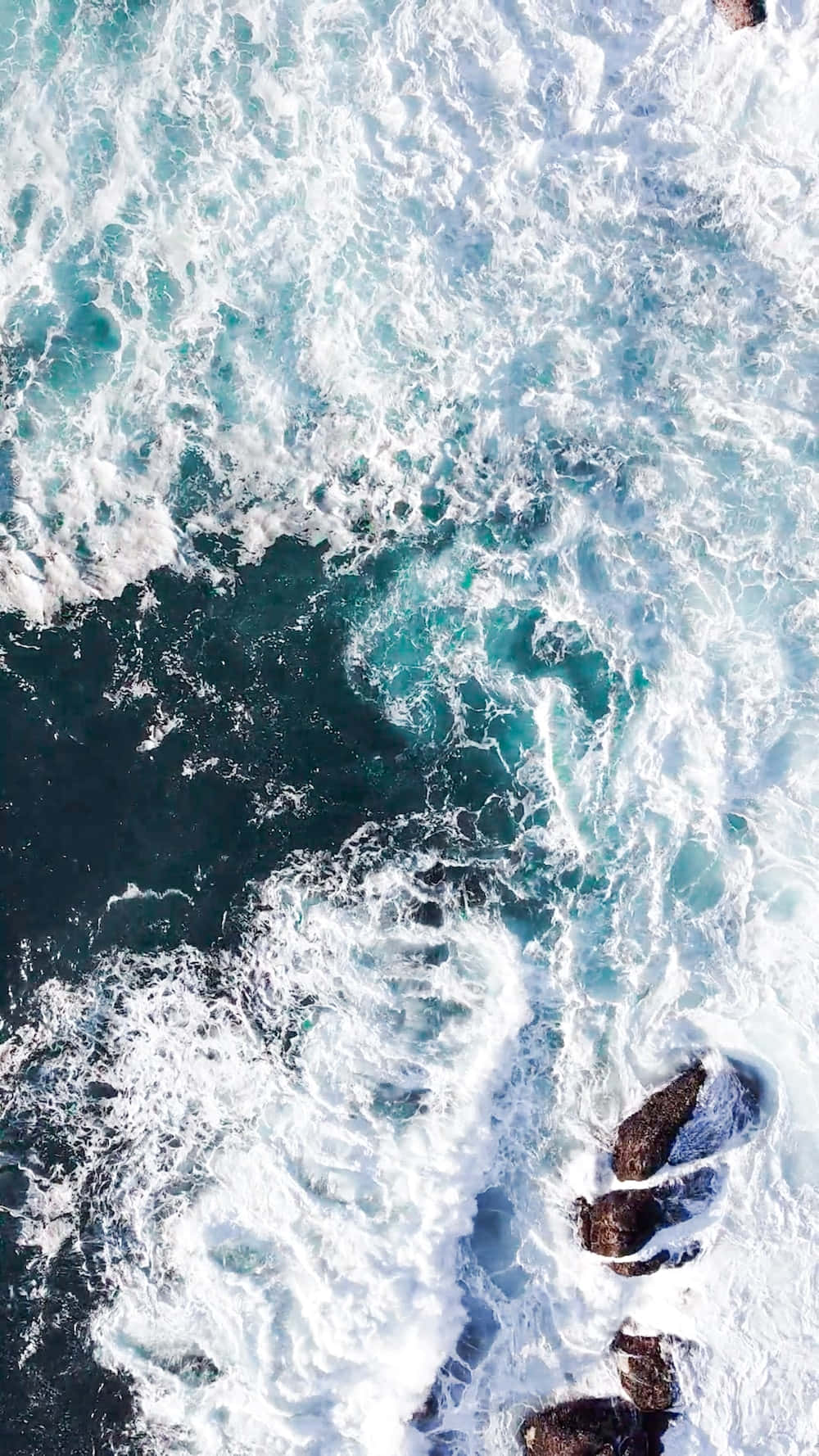 Sea Aesthetic 桌布 壁紙 — 從空中俯瞰，碧綠色的海浪拍打著黑色岩石，形成白色泡沫和漩渦水流。