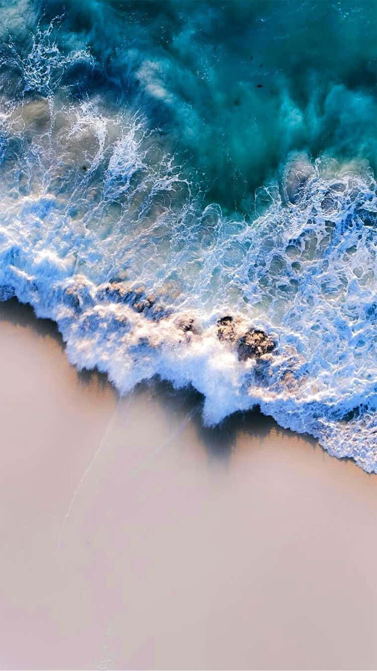 Cute Beach iPhone 桌布 壁紙 — 從空中俯瞰，綠松石色的海浪拍打著淺粉色的沙灘，泛起白色泡沫。