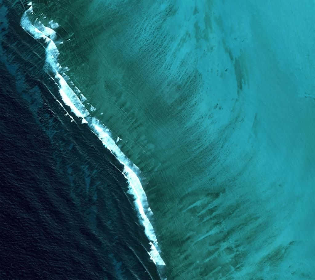 從空中俯瞰，海浪與沙灘交匯，呈現綠松石色的海水。 — Google pixel 壁紙