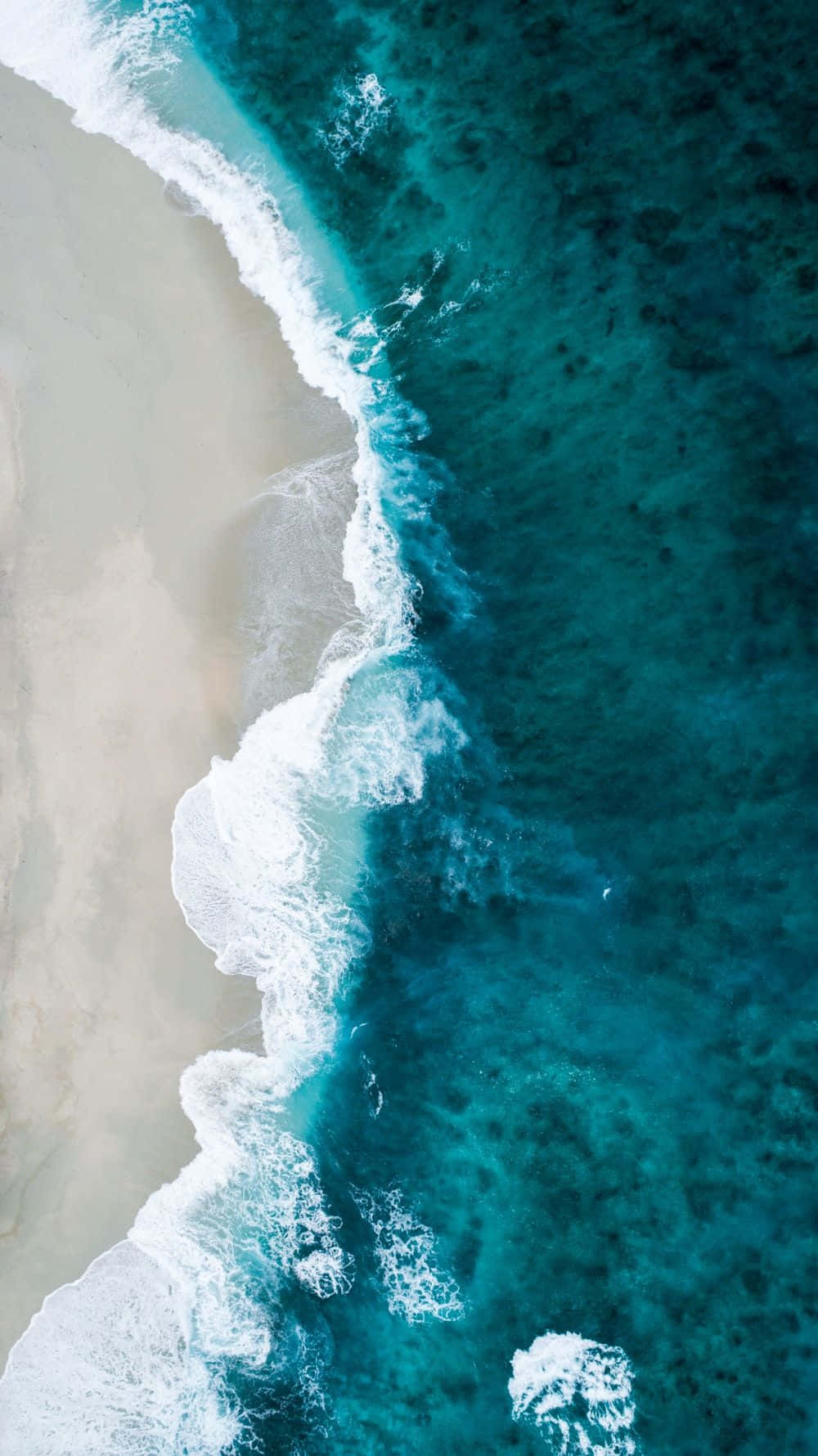 海洋藍 桌布 壁紙 — 從空中俯瞰，綠松石色的海浪拍打著淡色沙灘，形成對角線分割。