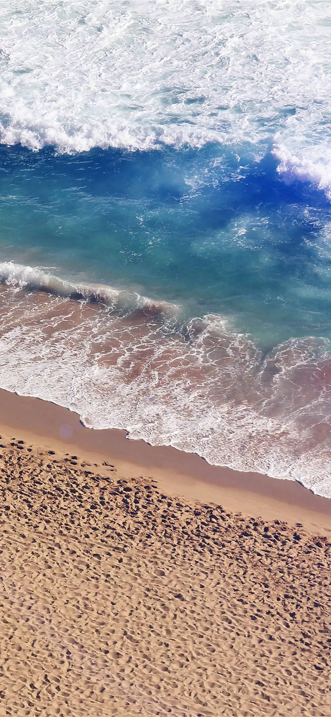 iPhone X Beach 桌布 壁紙 — 從空中俯瞰，藍綠色海浪拍打著質感沙灘，泛起白色泡沫。