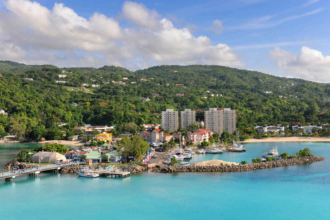 Jamaican Island 桌布 壁紙 — 從空中俯瞰一個充滿活力的熱帶港口，有碧綠的海水、船隻和點綴著建築物的茂密綠色山丘，天空部分多雲。