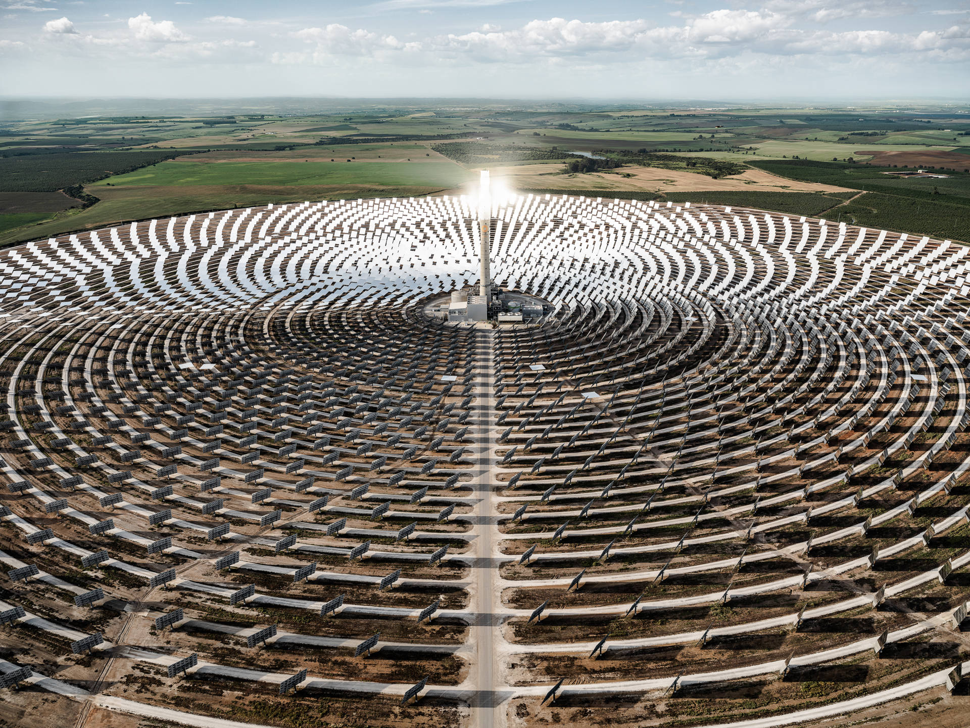 科技動圖 桌布 壁紙 — 從空中俯瞰一個巨大的太陽能發電廠，數千面鏡子在部分多雲的天空下向外輻射向中央塔。