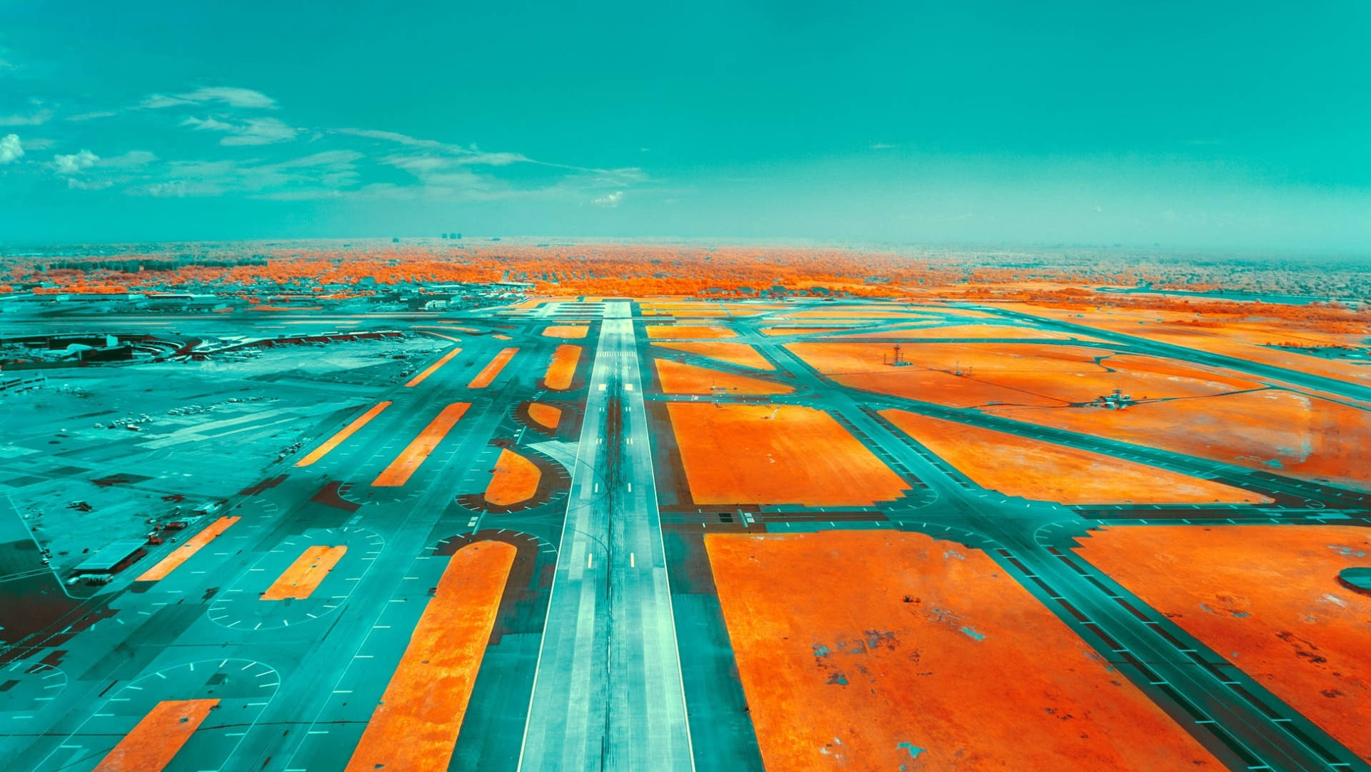 Runway 桌布 壁紙 — 從空中俯瞰一個廣闊的機場，在藍綠色天空下，橙色跑道和滑行道閃閃發光。
