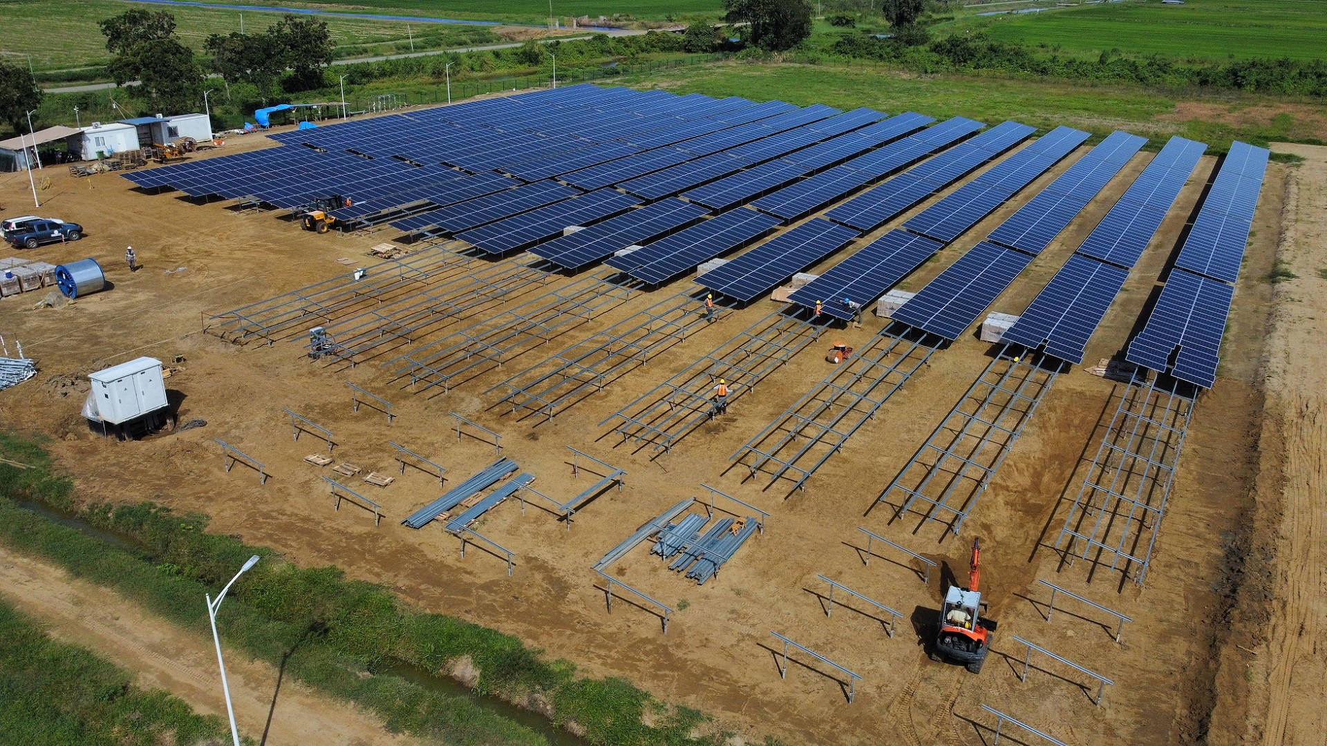 電力 桌布 壁紙 — 從空中俯瞰一個正在建設中的太陽能農場，工人和機械在一個被綠色田野包圍的泥土地上工作。
