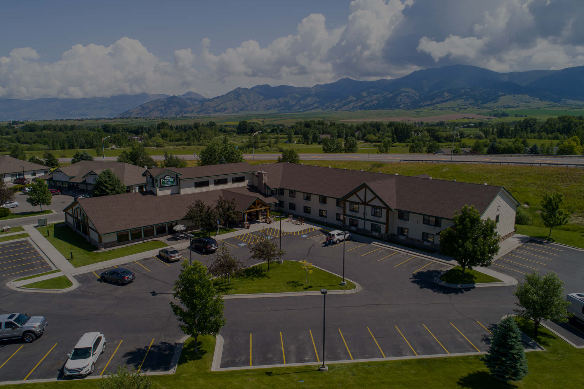 Mountain View 桌布 壁紙 — 從空中俯瞰一個酒店綜合體，停車場周圍是綠色田野和遠處的山脈，天空部分多雲。