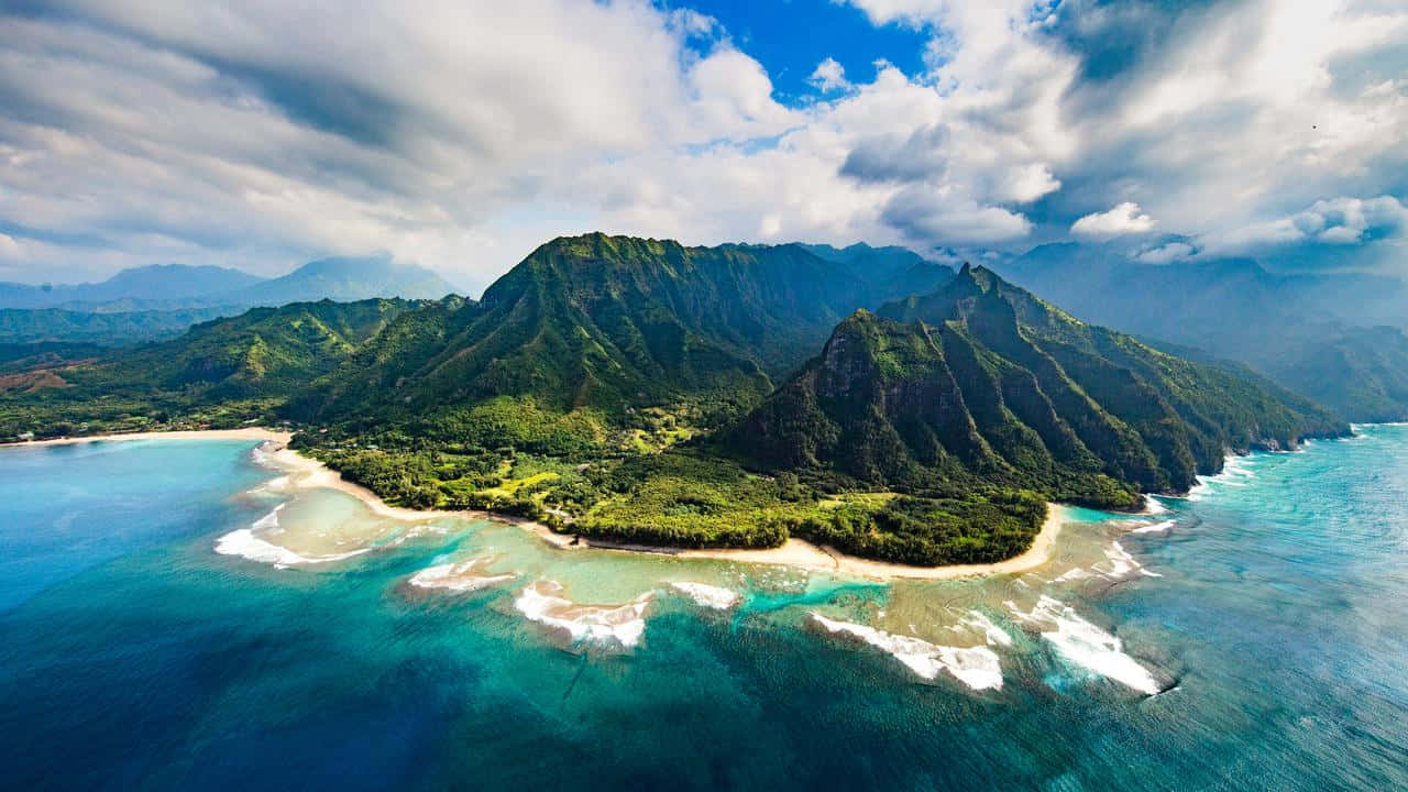 Hawaiian Island 桌布 壁紙 — 從空中俯瞰一個鬱鬱蔥蔥的綠色島嶼，擁有碧綠的海水和白色沙灘，天空部分多雲。